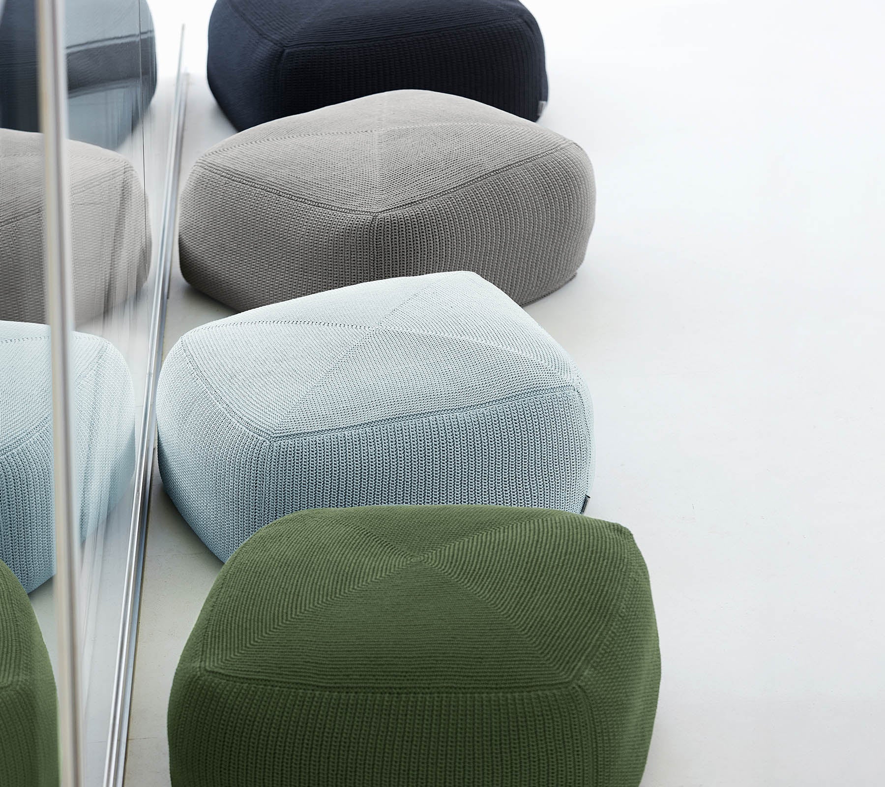 A collection of colorful, textured poufs in various shades, arranged together, reflecting stylish and modern design.