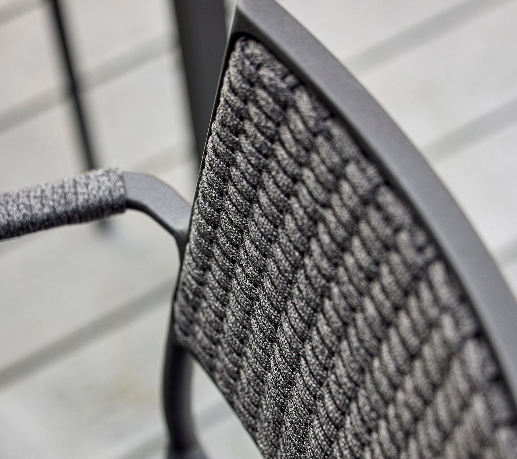 Close-up of a chair's backrest featuring a textured woven design and a sleek metal frame, emphasizing modern craftsmanship.