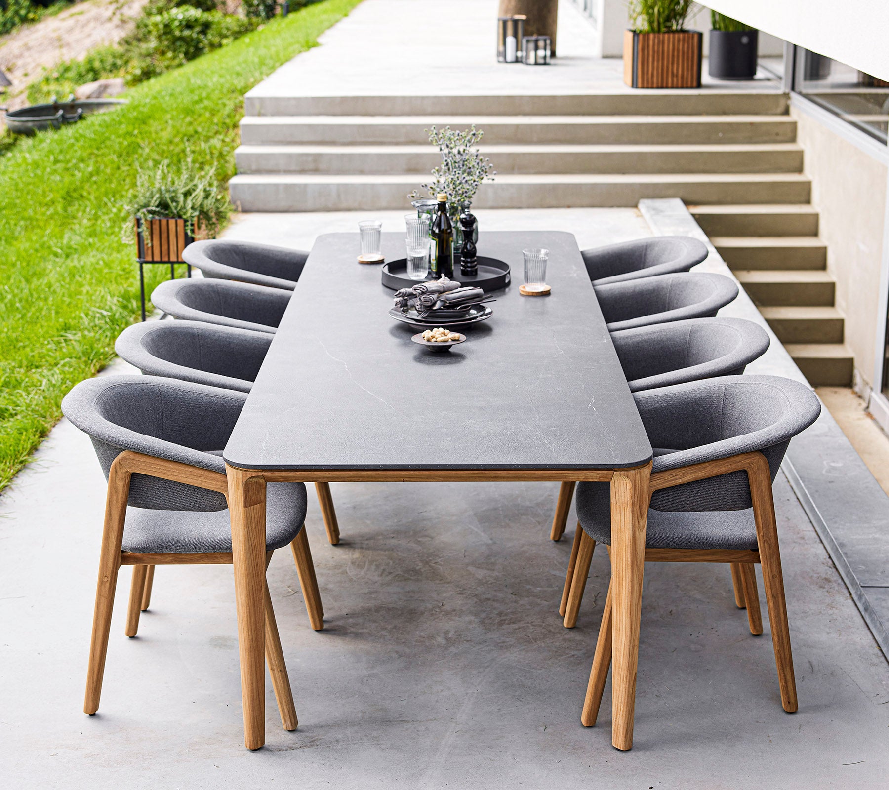 A modern dining table with eight gray chairs, featuring decorative items and plants on the table, set in an elegant outdoor space.