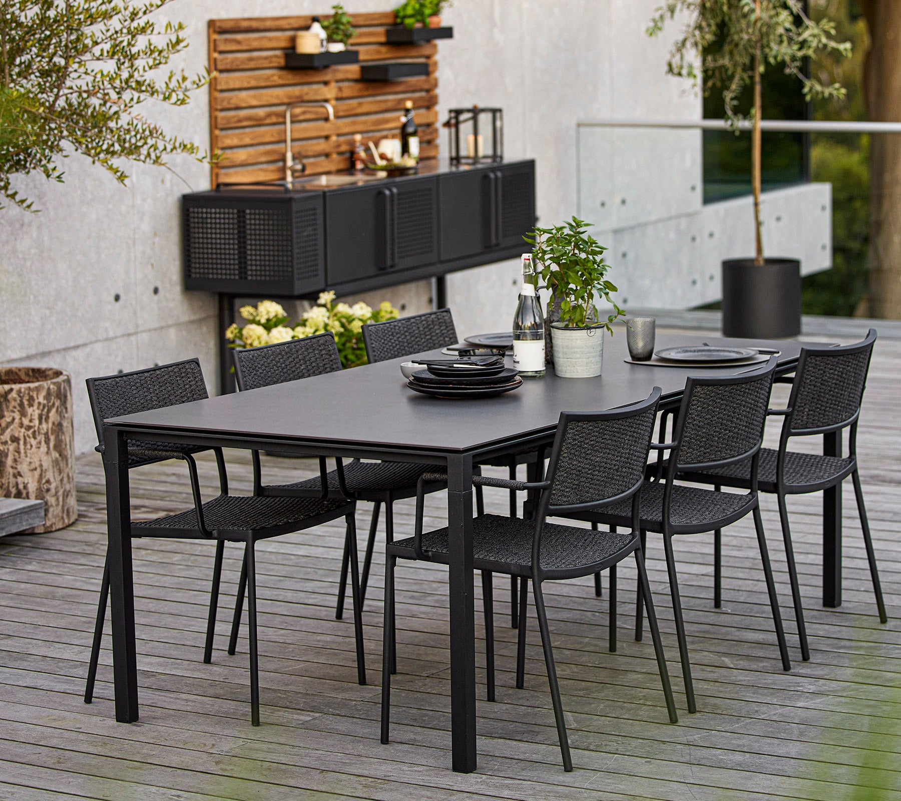 A modern dining set featuring a large rectangular table and six black woven chairs, accented by decorative elements and greenery.