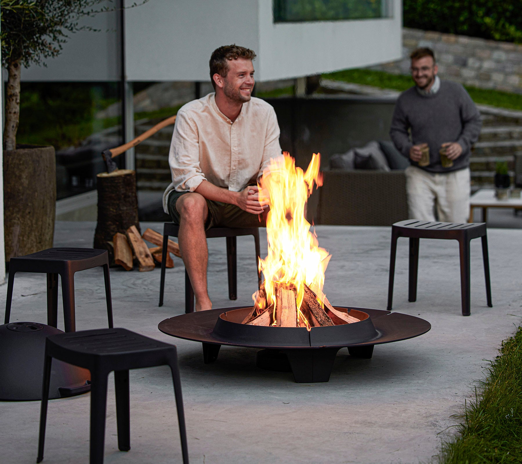 Two men enjoy a fire pit surrounded by modern seating, creating a cozy atmosphere for relaxation and conversation.