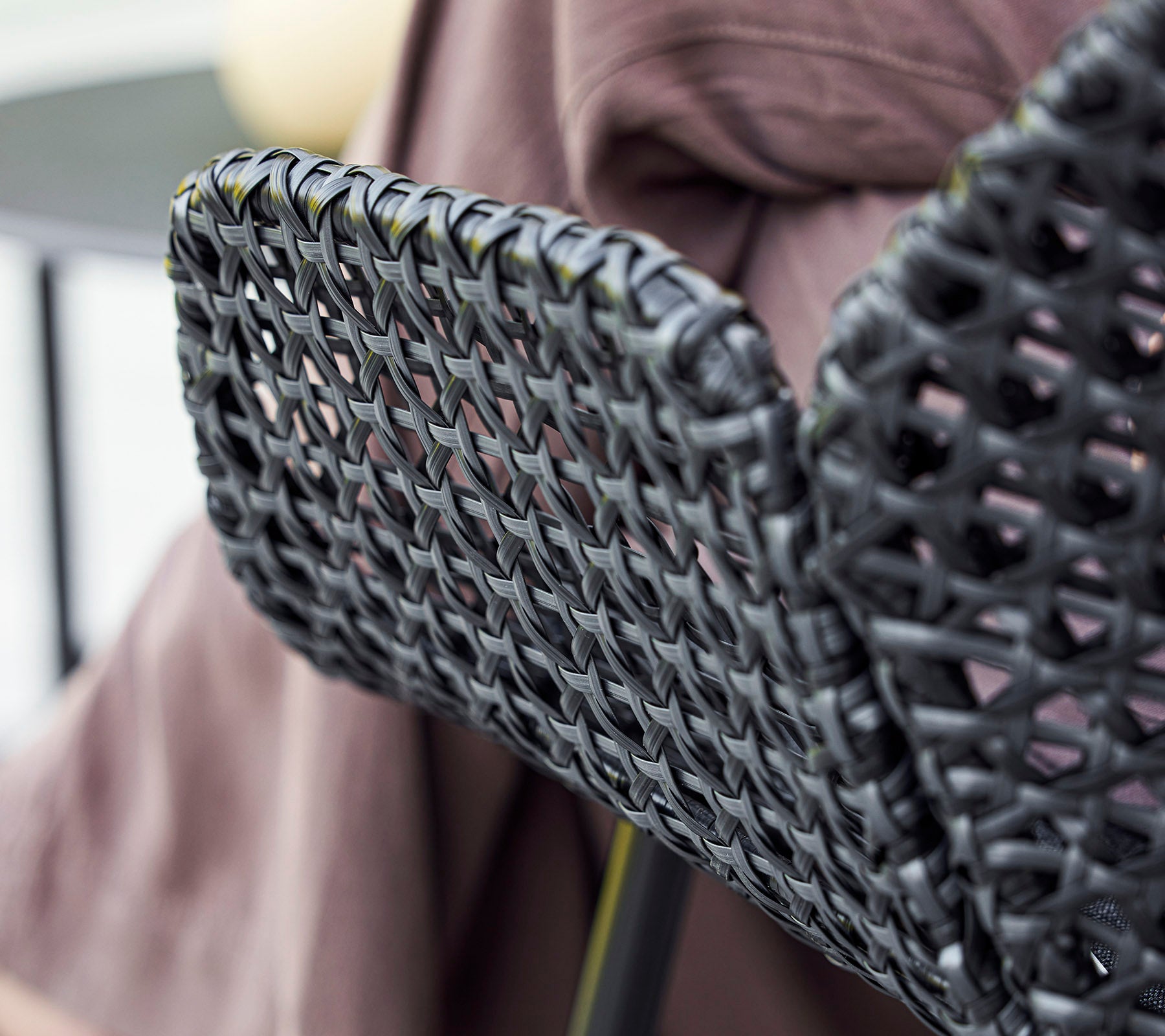 Black woven chair back with a textured design, complemented by a draped fabric in the background.