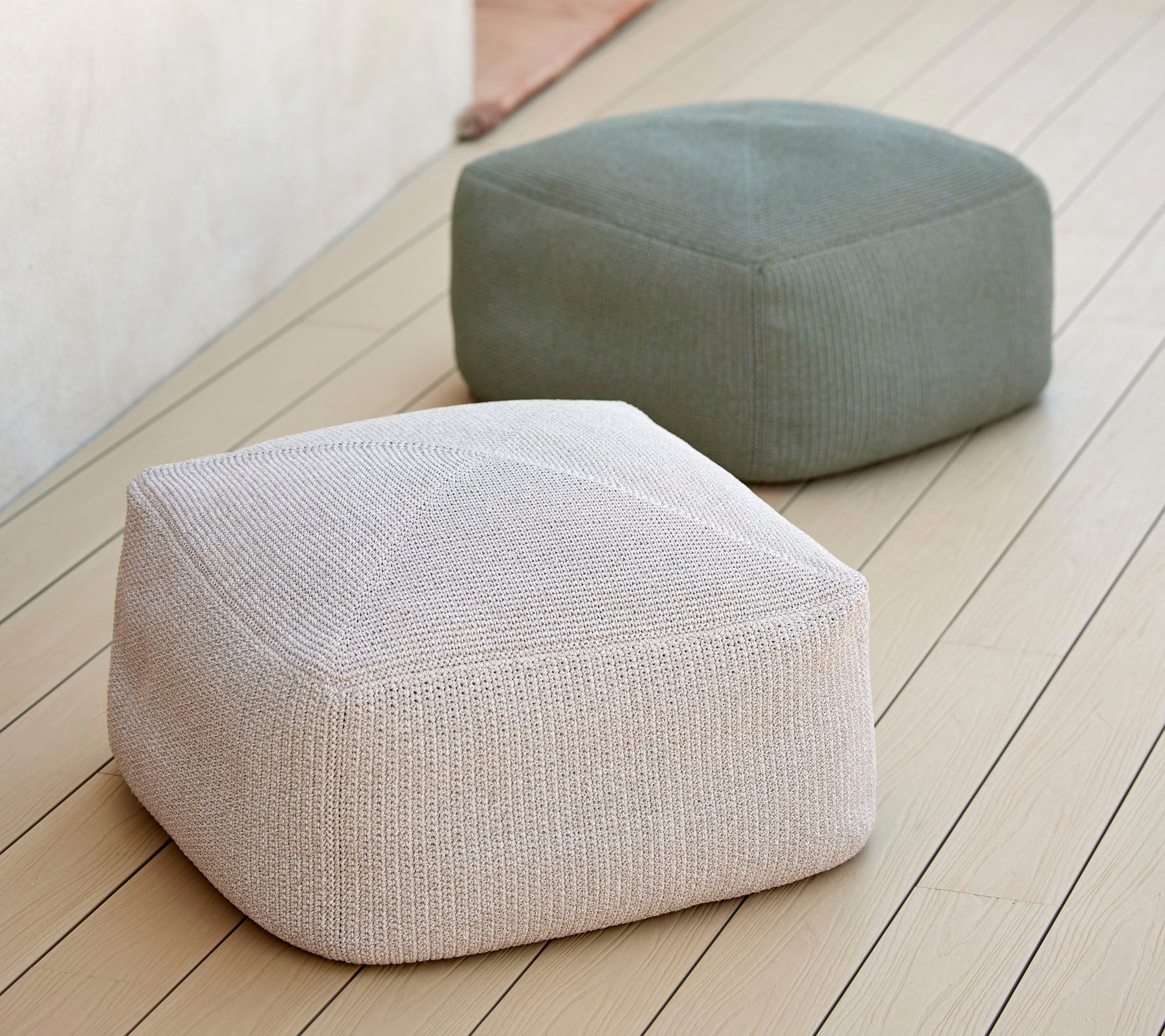 Two stylish, textured poufs in neutral tones, one white and one green, arranged on a smooth surface, ideal for versatile seating.