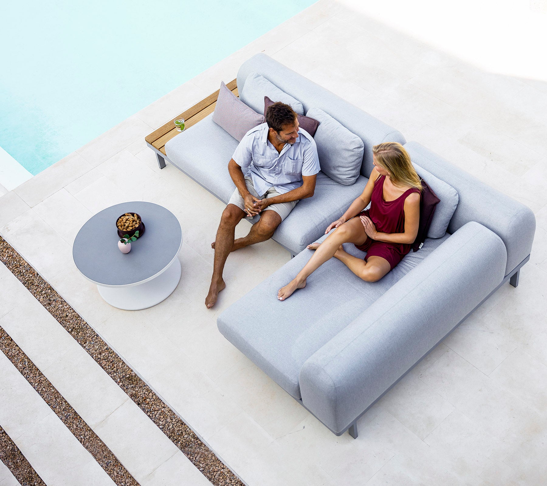 A man and woman are seated on a modern gray sofa, engaged in conversation, with a small table and decorative items nearby.