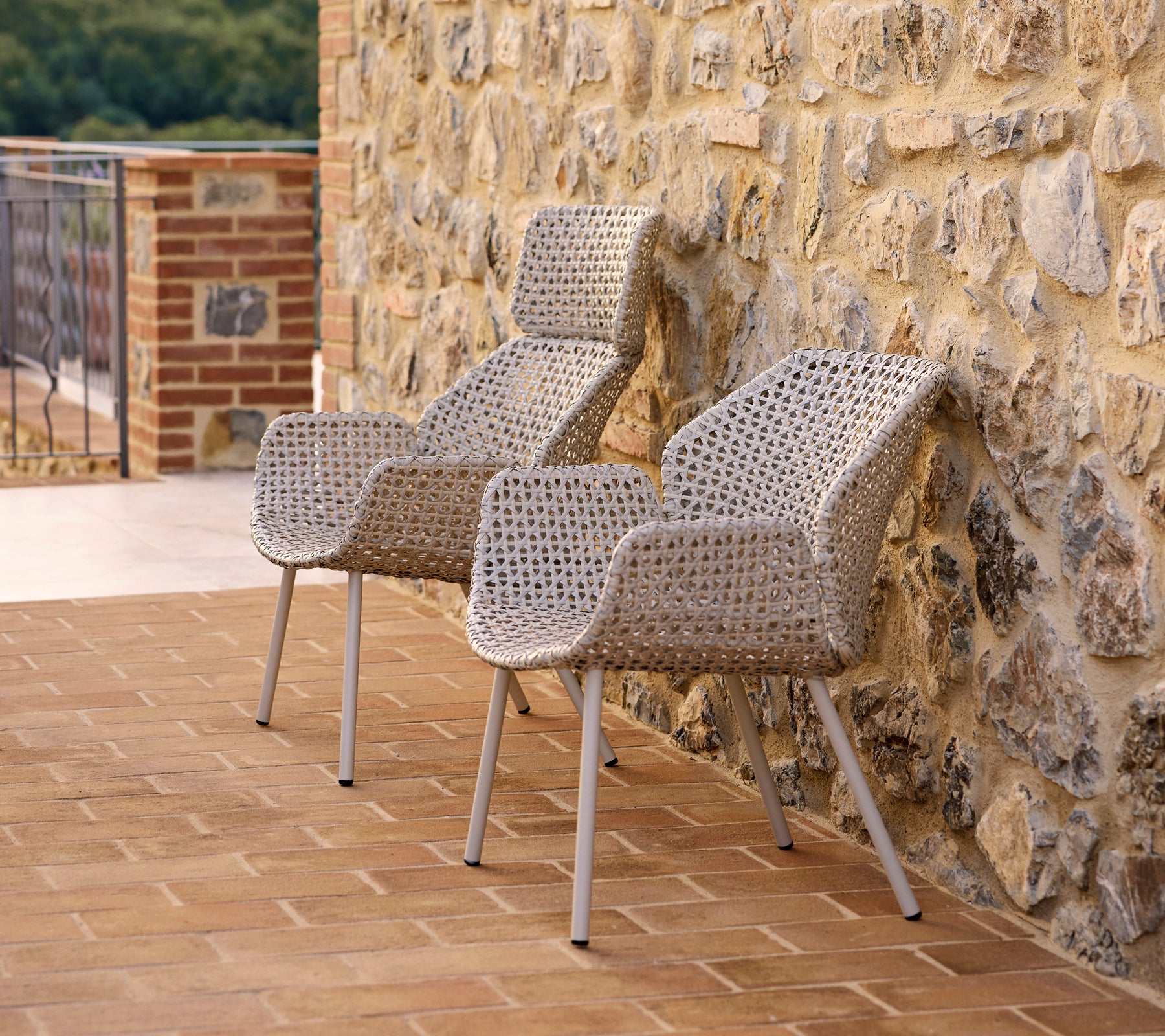 Two stylish Vibe highback lounge chairs made of woven material, positioned against a stone wall, perfect for relaxation.