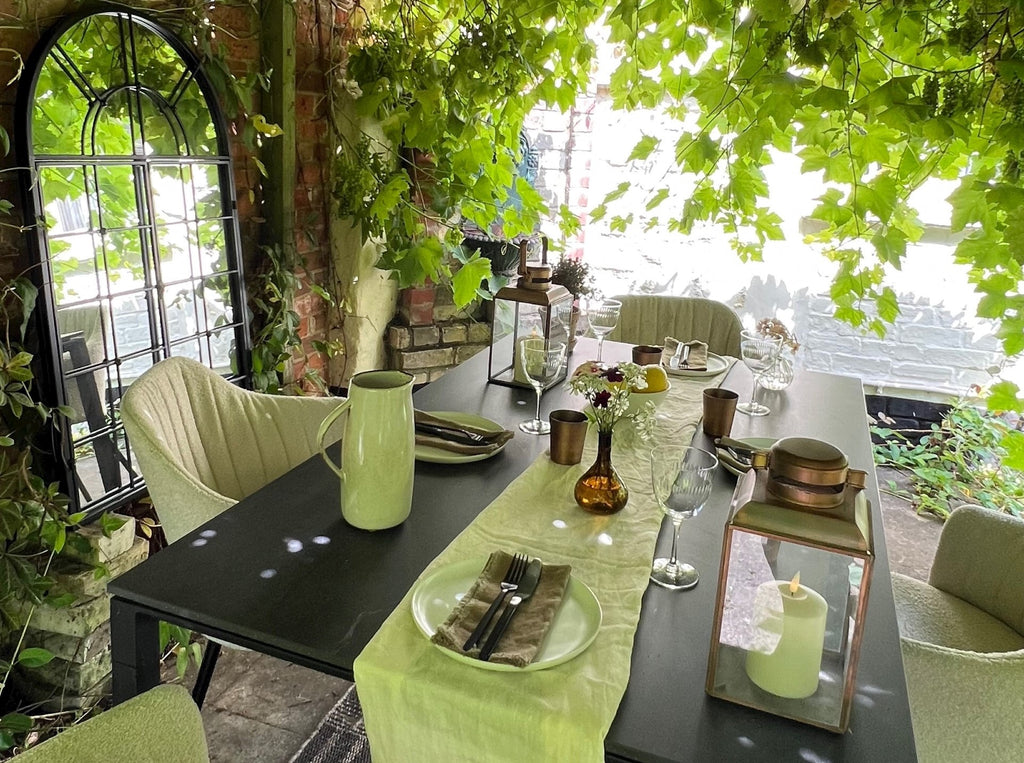 Lush green pergola with grapevine decoratede with a modern dining setting with black outdoor dining table and sand bouclé dining chairs 