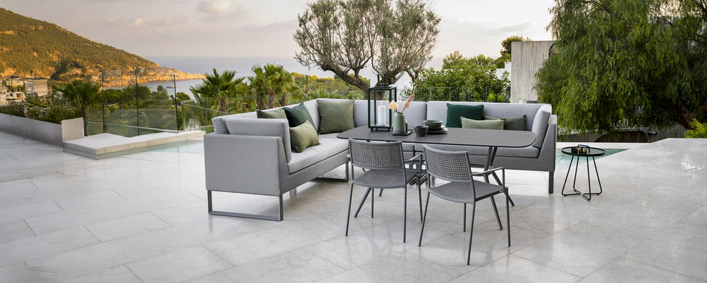 Modern outdoor lounge area with grey sofa, green cushions, black table, and grey chairs.