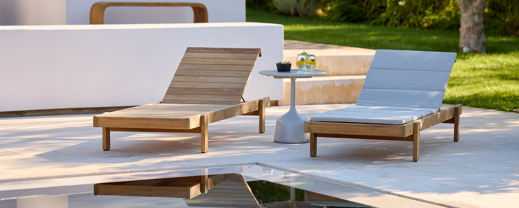 Modern outdoor lounge area with wooden chairs and white side table.