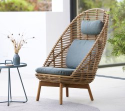 Stylish woven chair with a high backrest, padded seat, and matching cushion, accompanied by a small table and decorative vase.