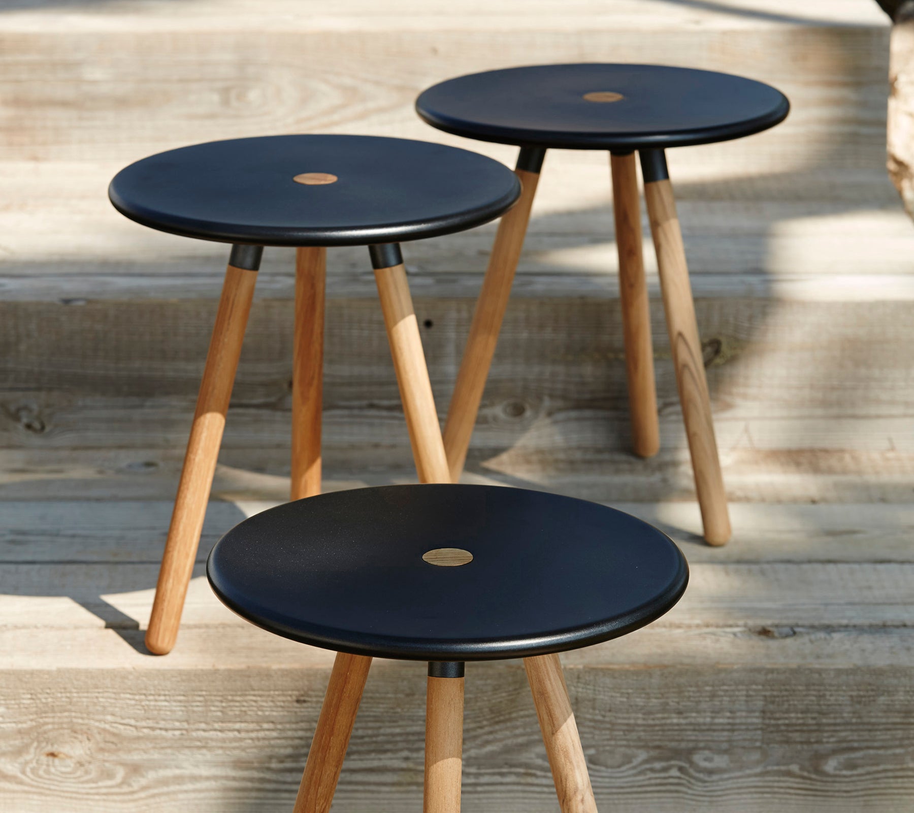 Three modern black stools with wooden legs on a wooden surface.