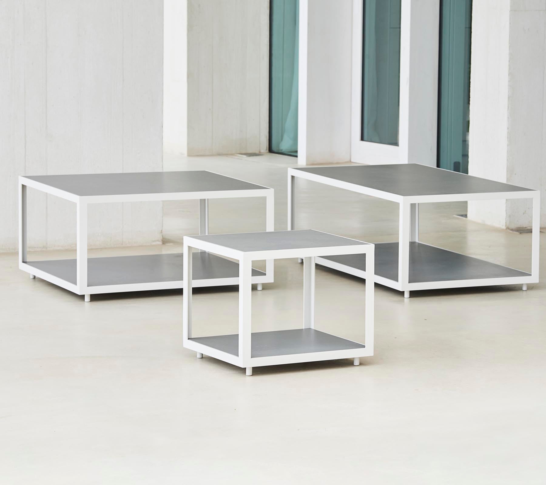 A set of three modern tables with a sleek design featuring metal frames and flat surfaces, arranged in varying sizes.
