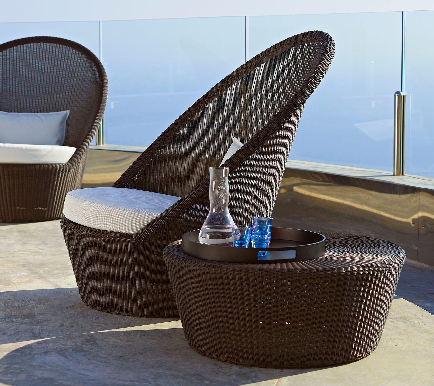 Stylish brown wicker chair with a high back and white cushion, accompanied by a matching side table and decorative items.