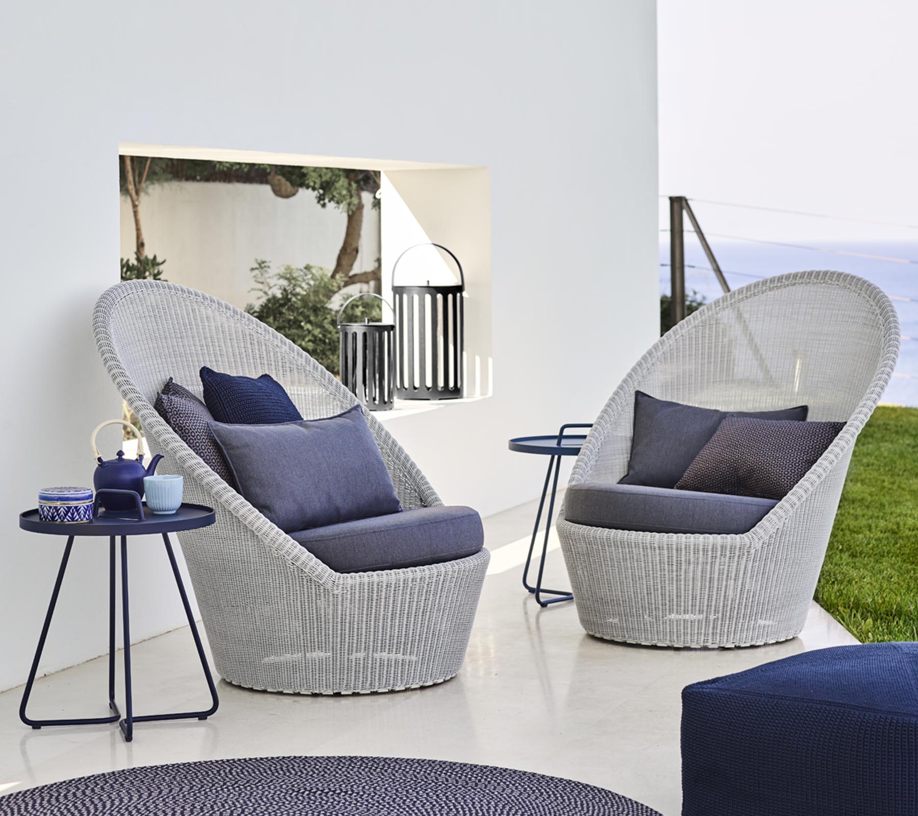 Two stylish woven lounge chairs with blue cushions alongside a small table, set against a serene backdrop.