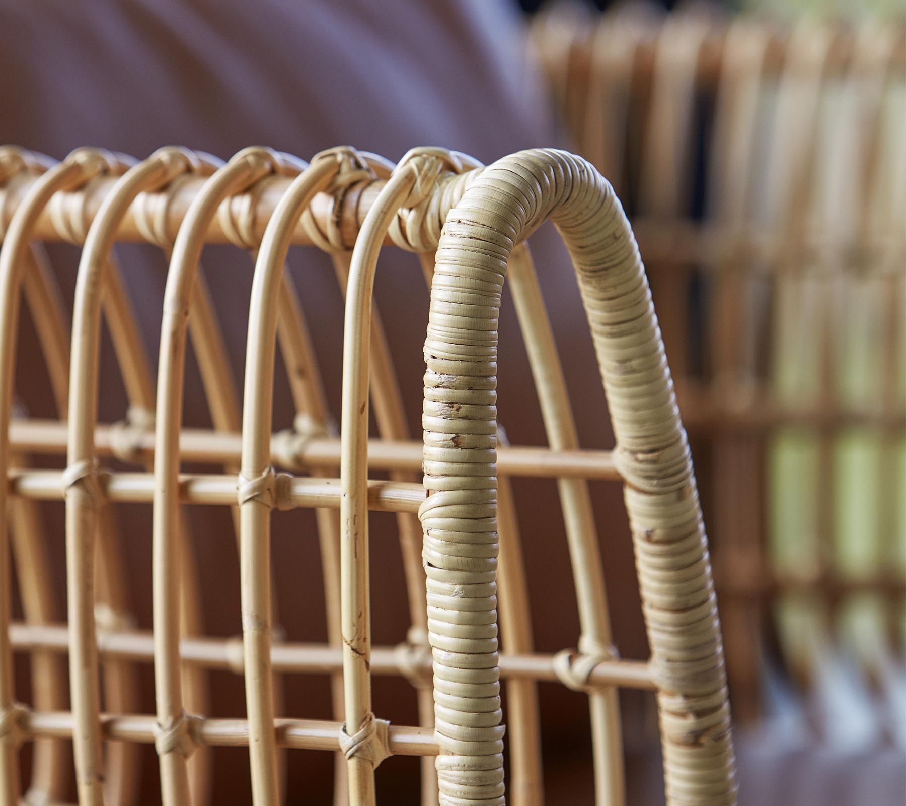 Close-up of a woven rattan chair, featuring curved lines and a natural finish, highlighting its craftsmanship and design.