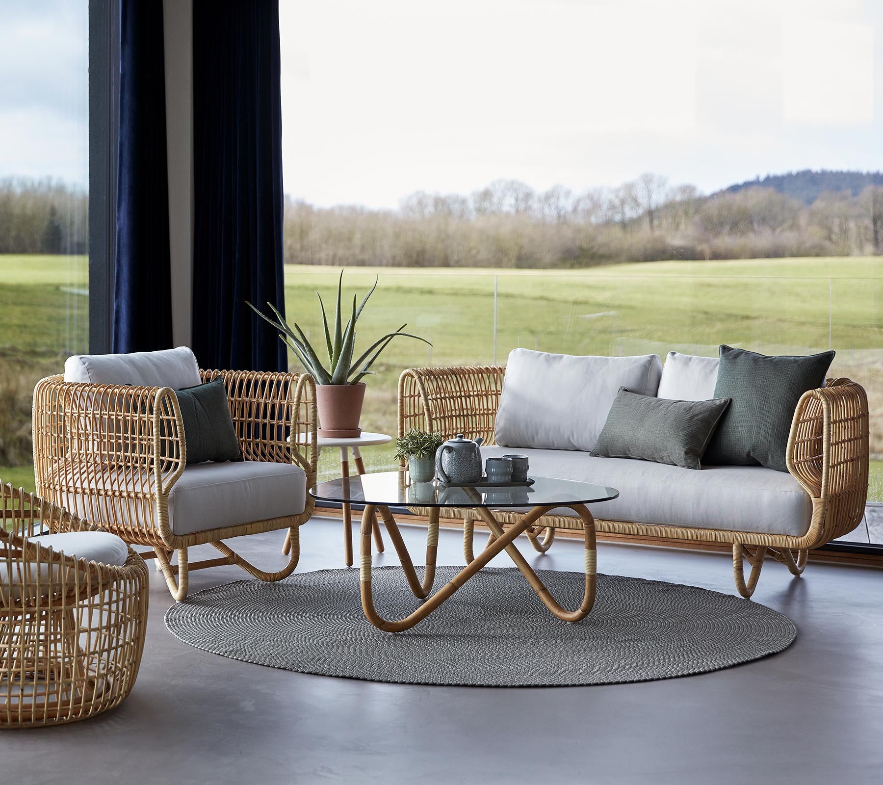 A stylish seating arrangement featuring woven furniture, a round rug, and a glass coffee table, complemented by minimalist decor elements.