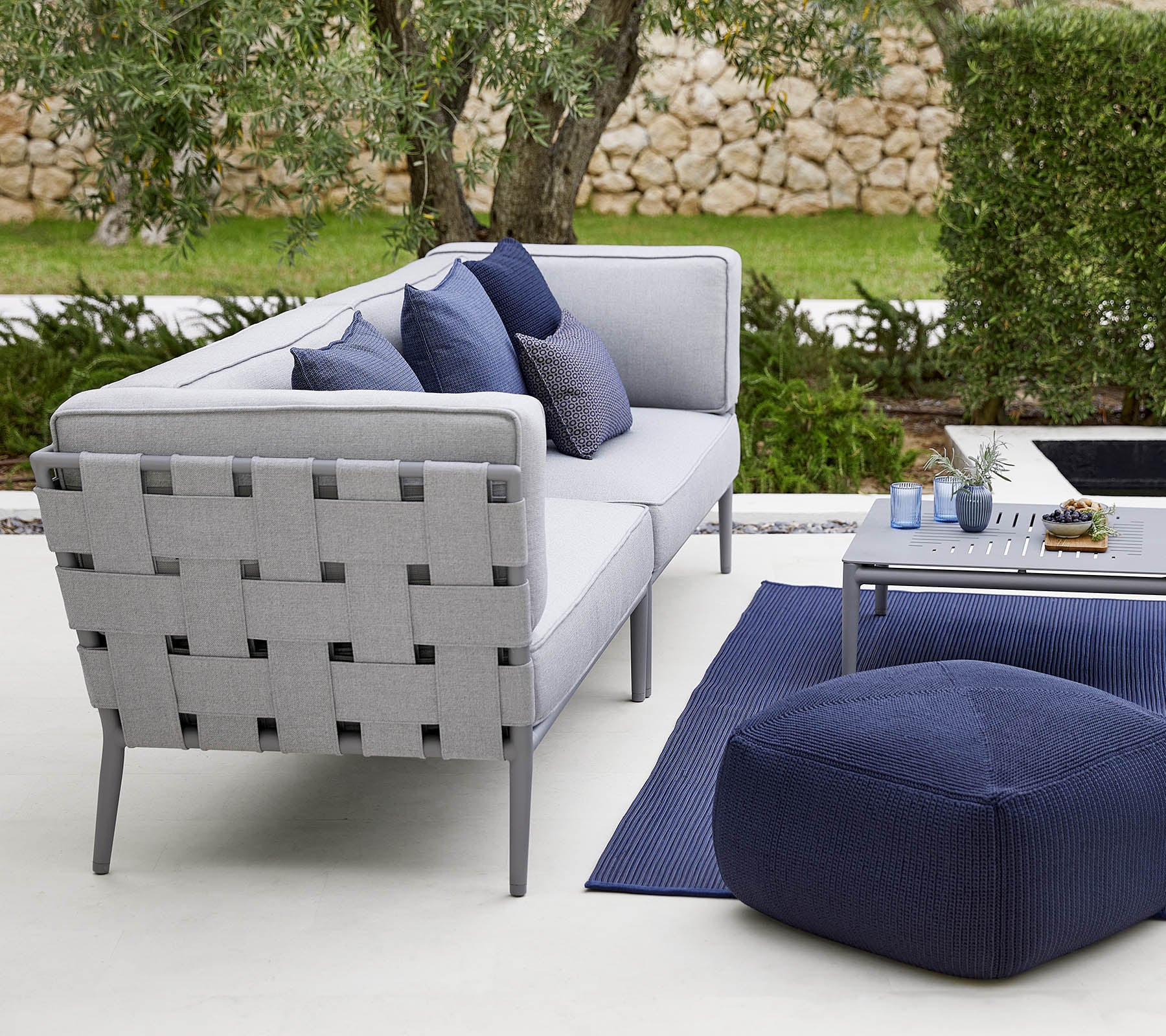 Modern outdoor seating arrangement featuring a gray sofa with decorative cushions, a stylish coffee table, and a cozy pouf.