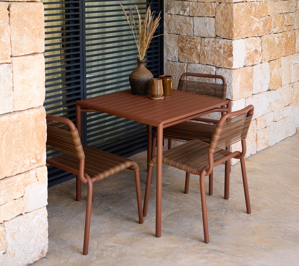 Brown table and chairs in a modern outdoor setting with stone walls.