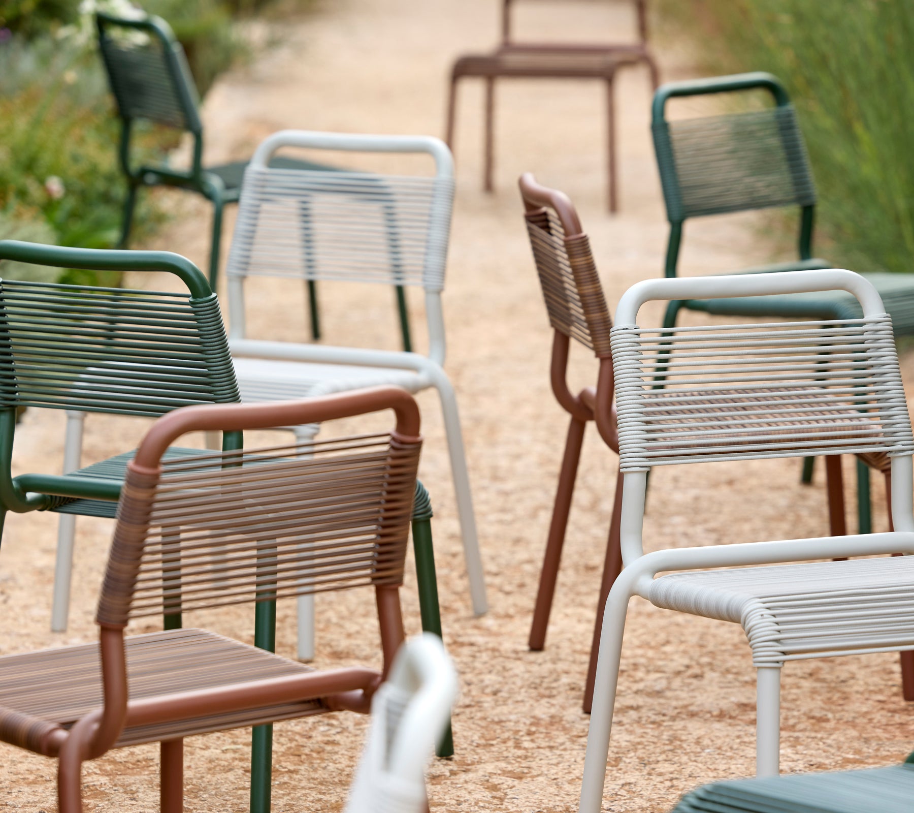Array of modern chairs in green, grey, brown, and white on a gravel pathway.
