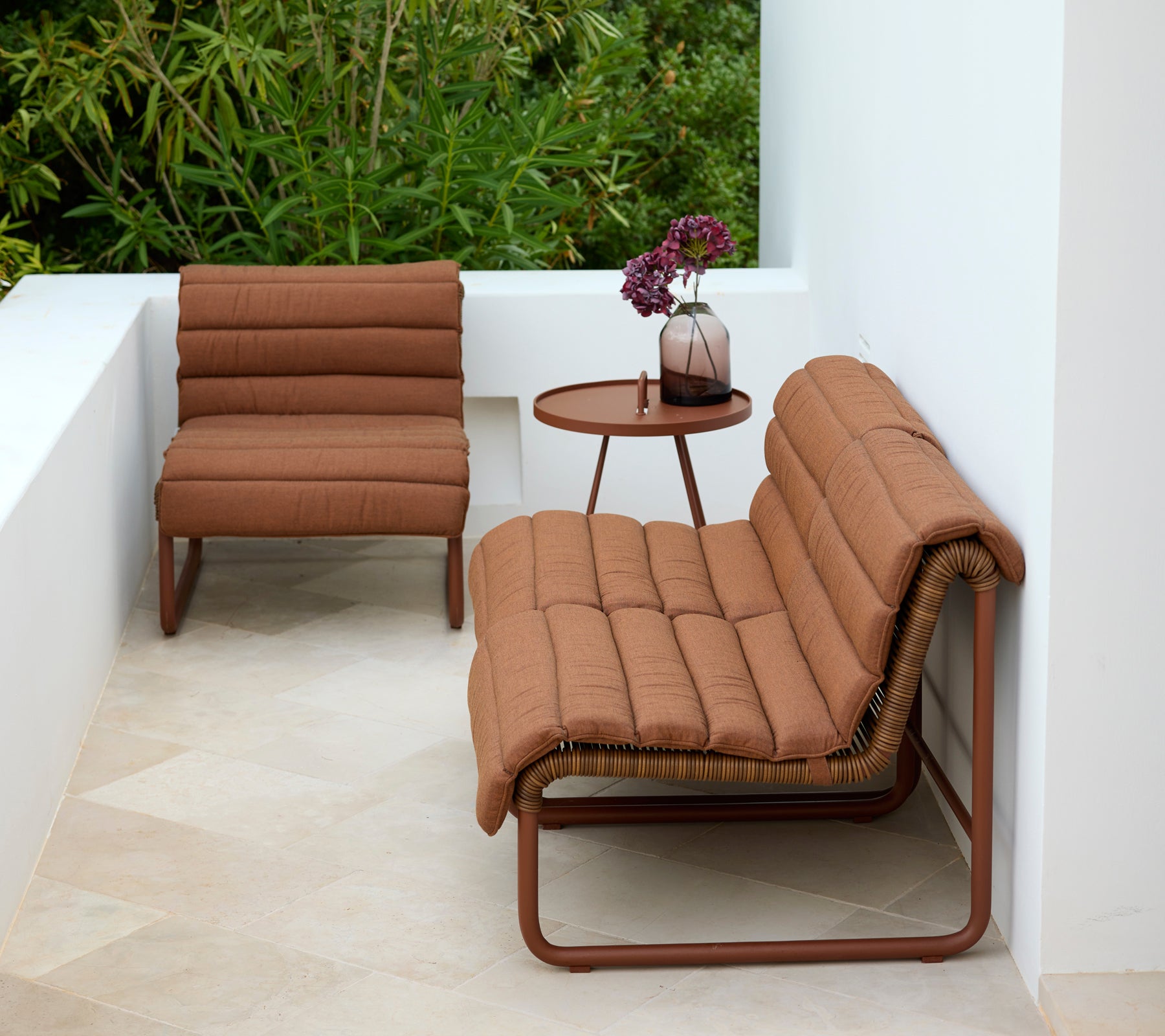 Brown lounge chair and loveseat with a round side table in a modern outdoor setting.