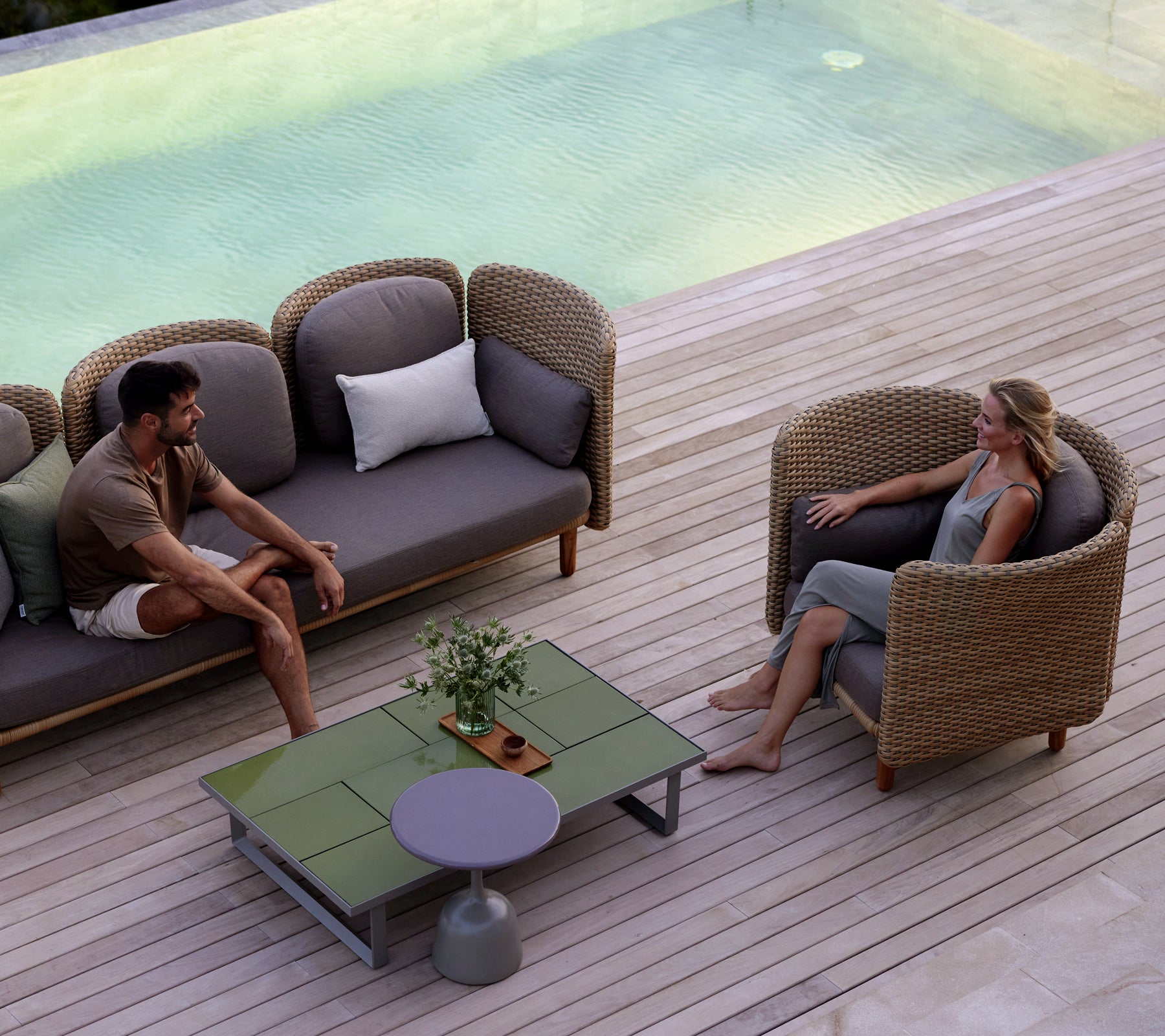 Two people seated in comfortable lounge chairs around a stylish coffee table, with a serene water feature in the background.