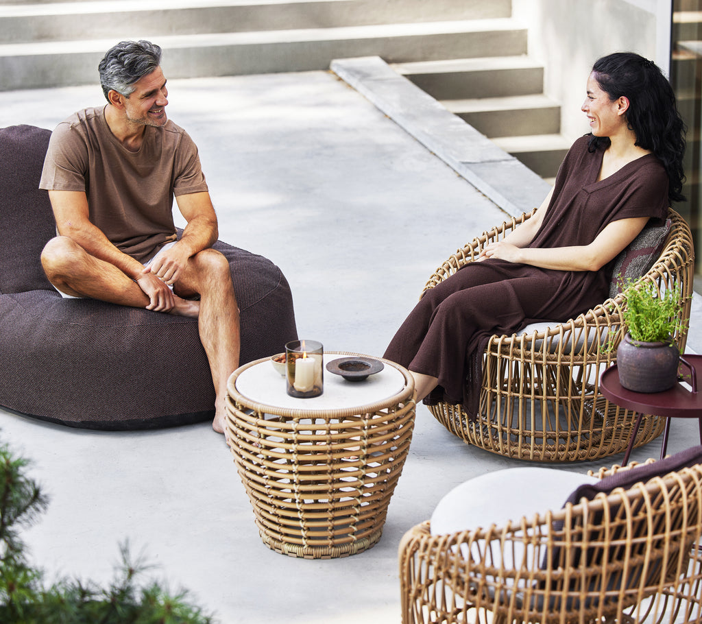 Two people sitting together, one on a cozy lounge chair and the other on a nest round chair, with a small basket coffee table between them.
