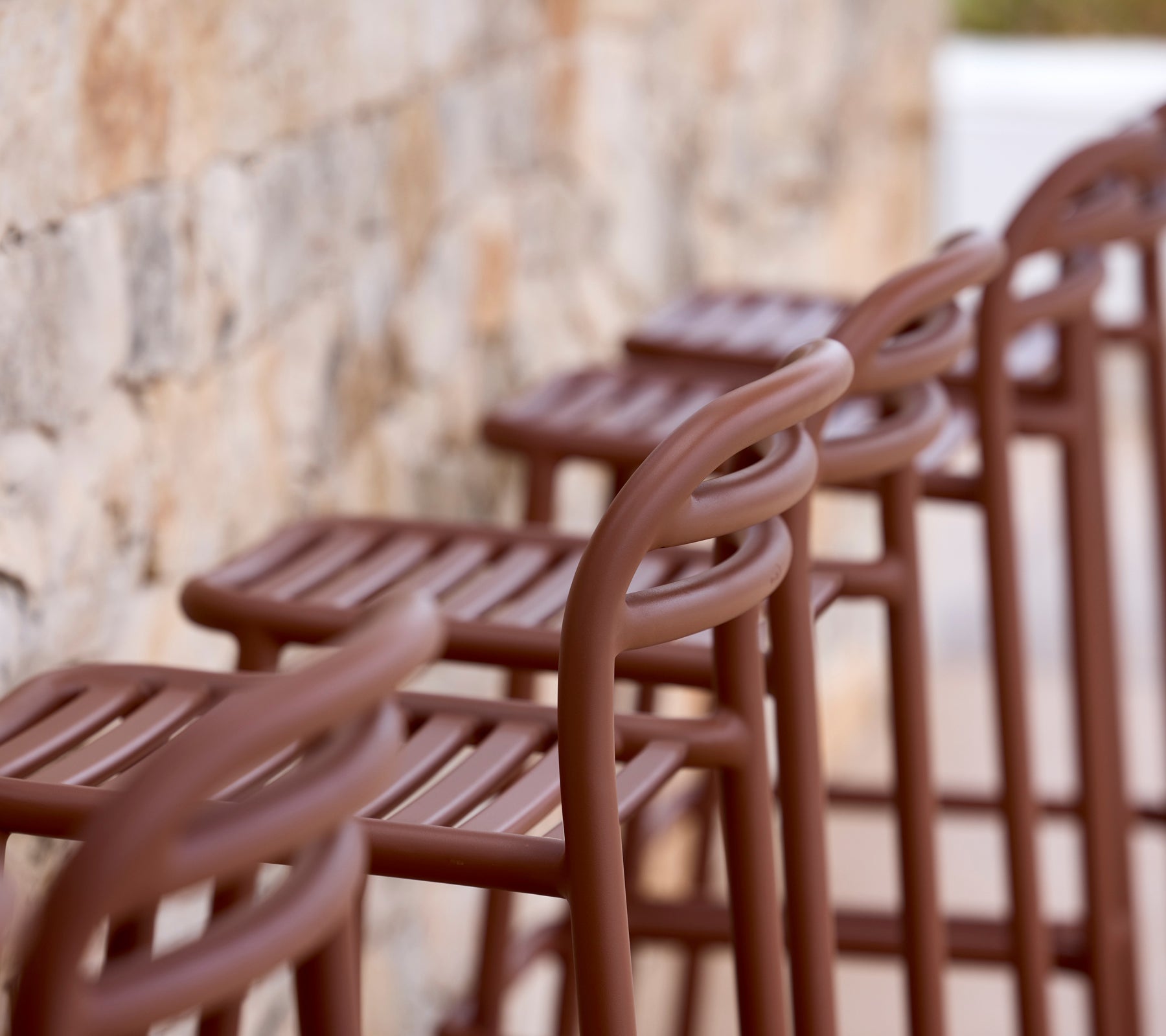 Row of brown bar stools against a stone wall.