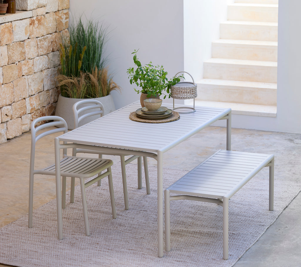 Light grey dining set including a table, chairs, and bench in a modern outdoor setting.