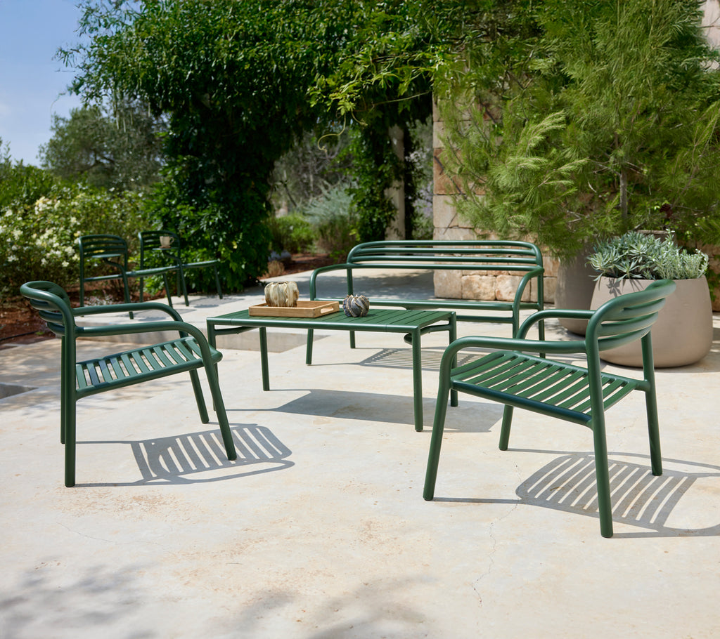 Green outdoor seating arrangement with chairs and bench surrounding a table.