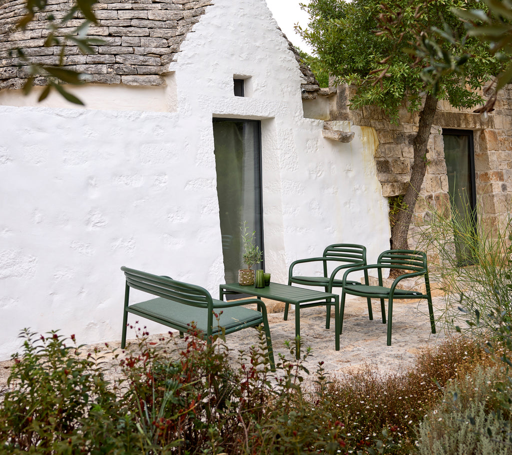 Green outdoor sofa and armchairs with a coffee table in a cozy setting.