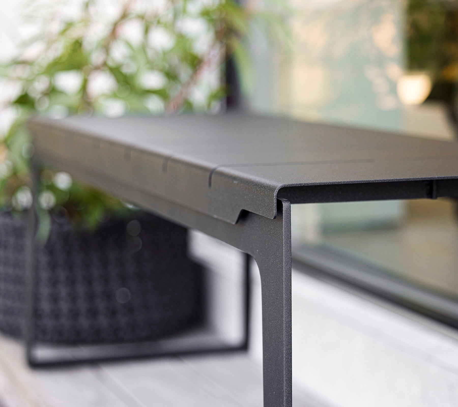 Sleek black table with a minimalist design, featuring clean lines and a sturdy frame, complemented by greenery in the background.