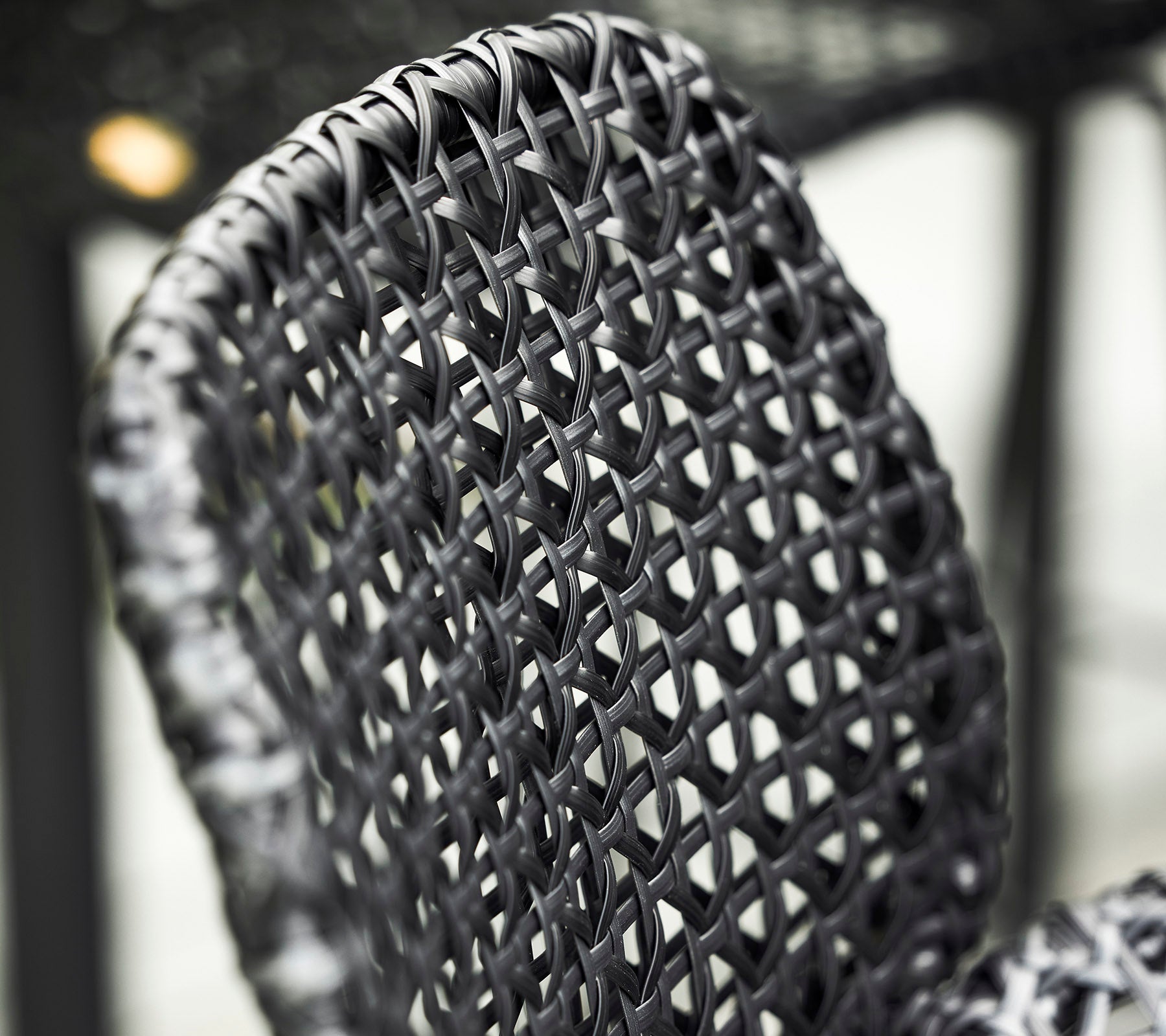 Close-up of a woven black chair backrest, showcasing intricate patterns and textures in its design.