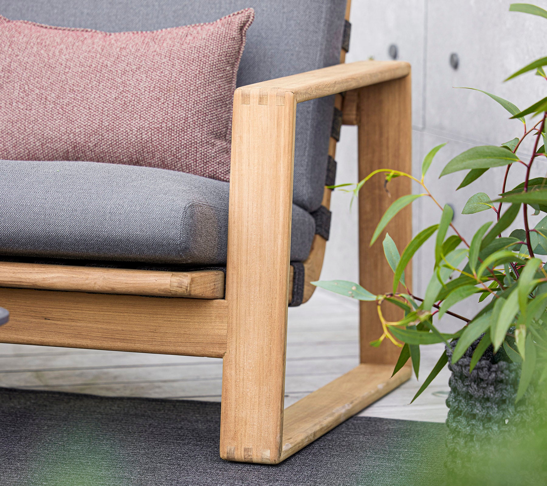 A modern sofa with a wooden frame, featuring gray cushions and a decorative pillow, complemented by lush green plants nearby.