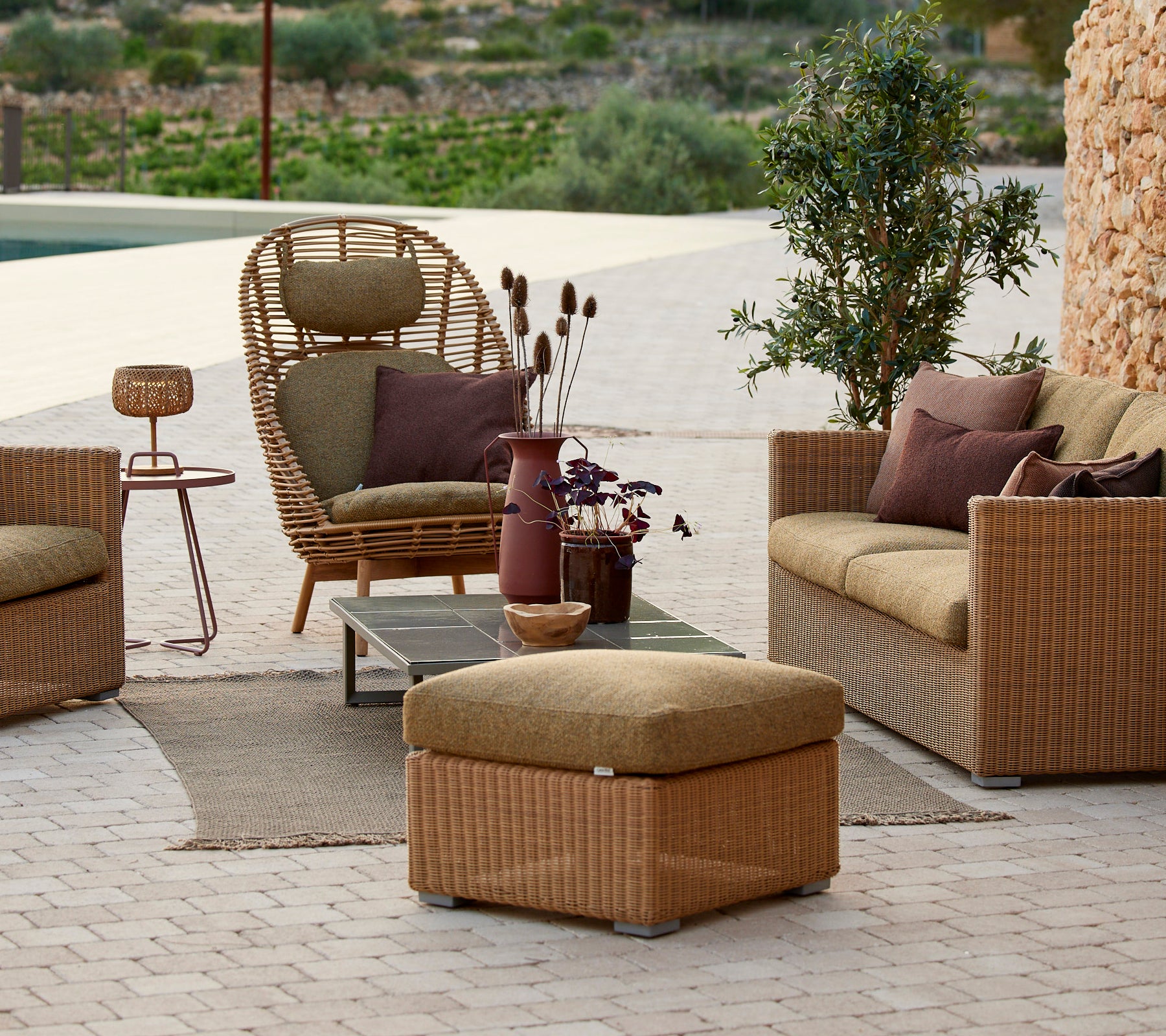 Lounge seating area featuring rattan chair, beige sofa, and side table with a purple vase.