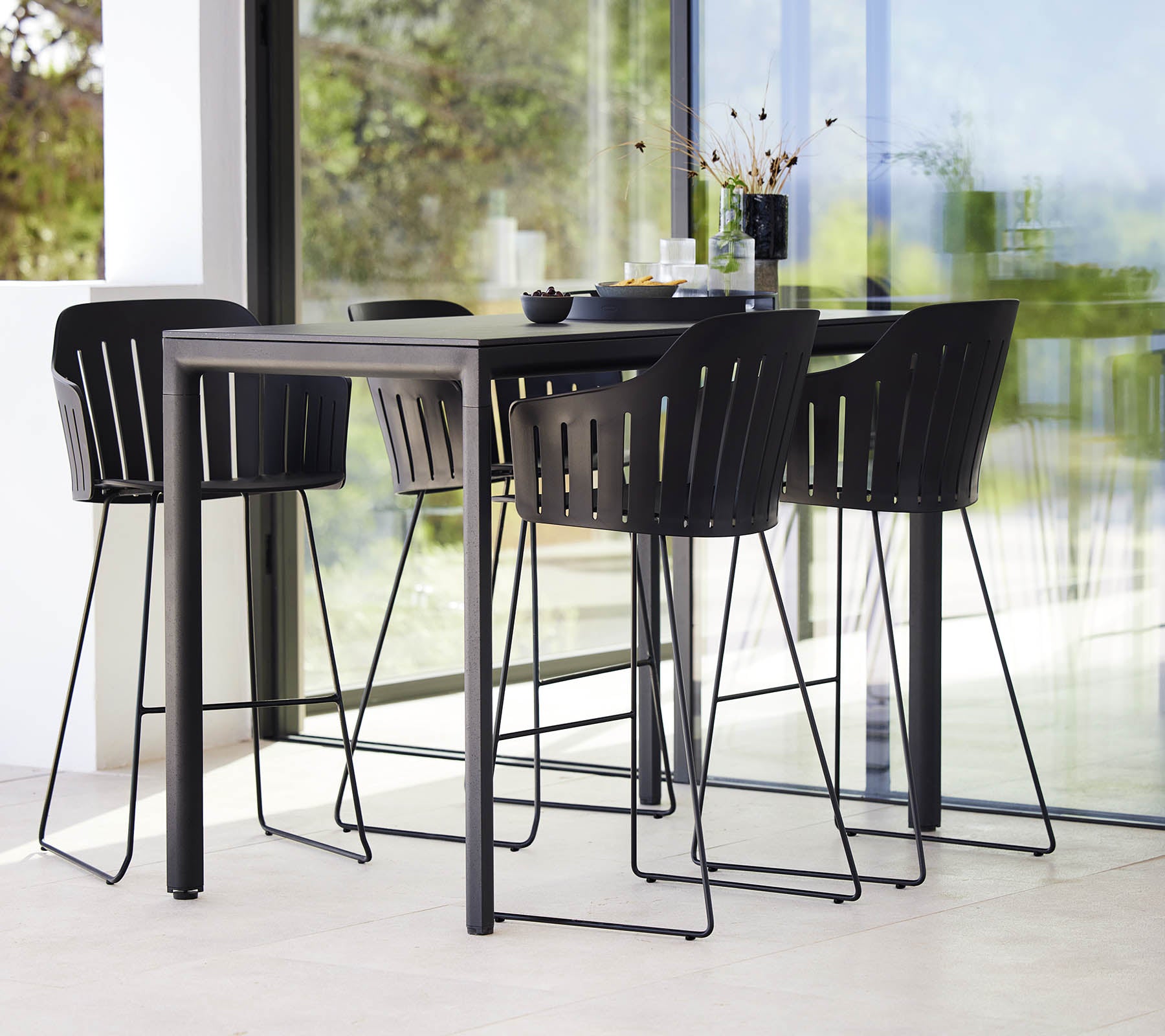 A sleek black bar table paired with modern bar chairs featuring a slatted design, creating a stylish seating arrangement.
