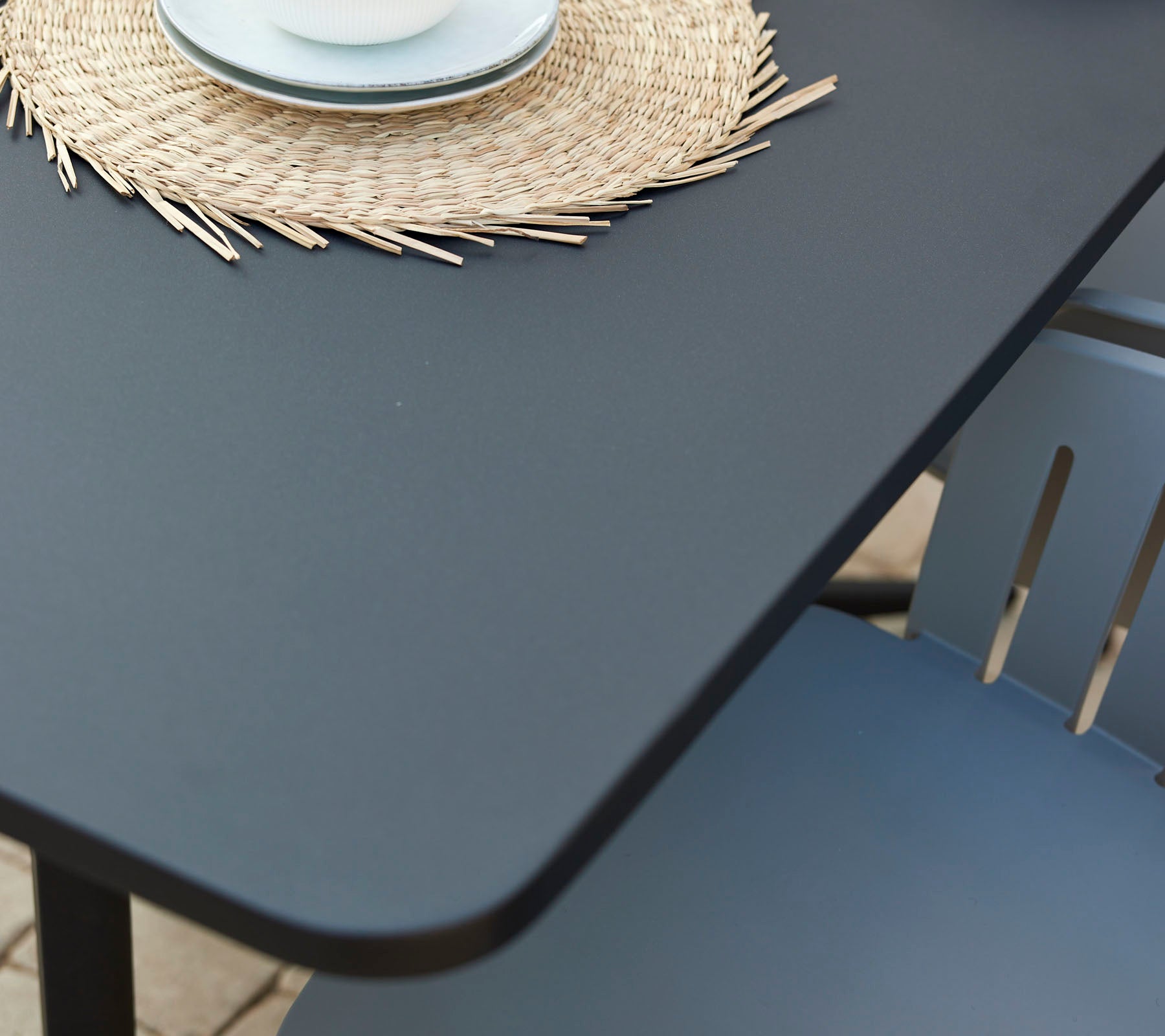 A modern café table with a smooth surface, accompanied by a decorative round placemat and a cup on a cozy chair.
