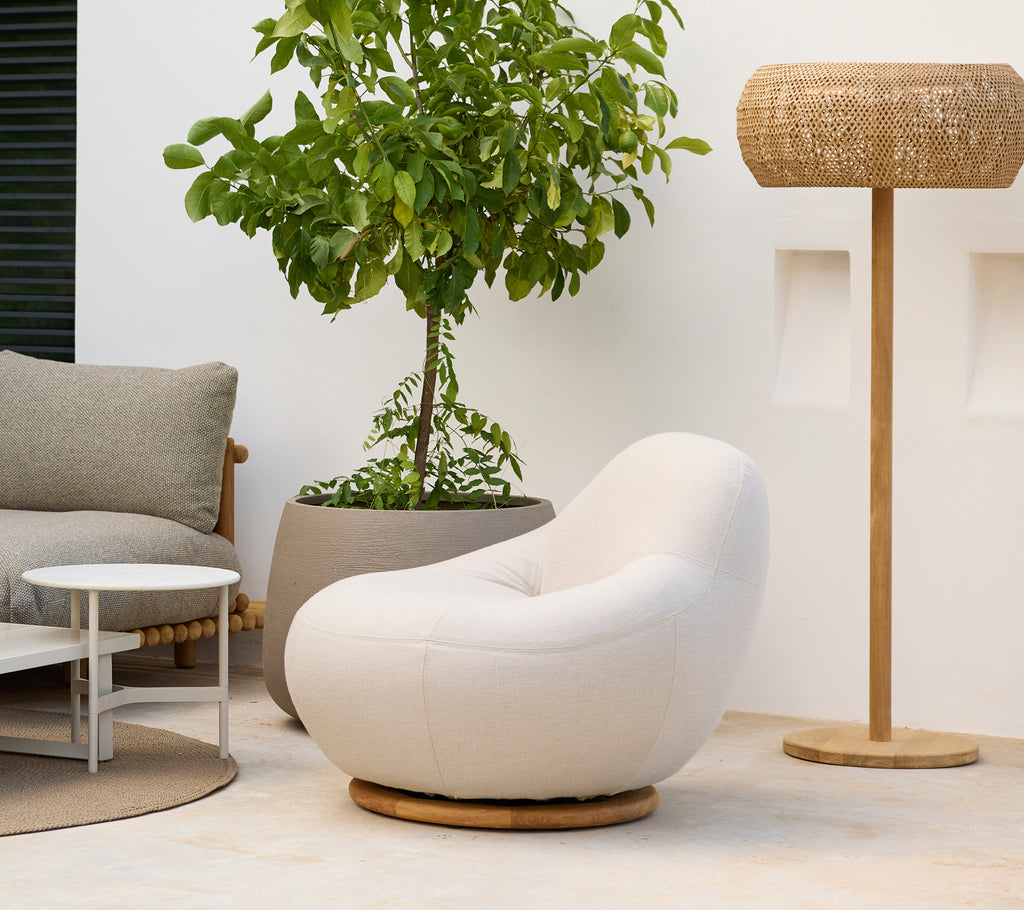 Modern lounge setup with a white chair, grey cushion, round coffee table, and woven lamp.