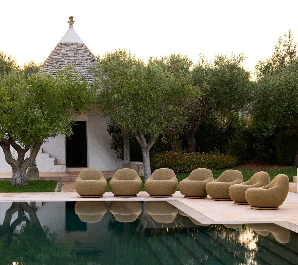Beige lounge chairs arranged by a poolside with olive trees in the background.