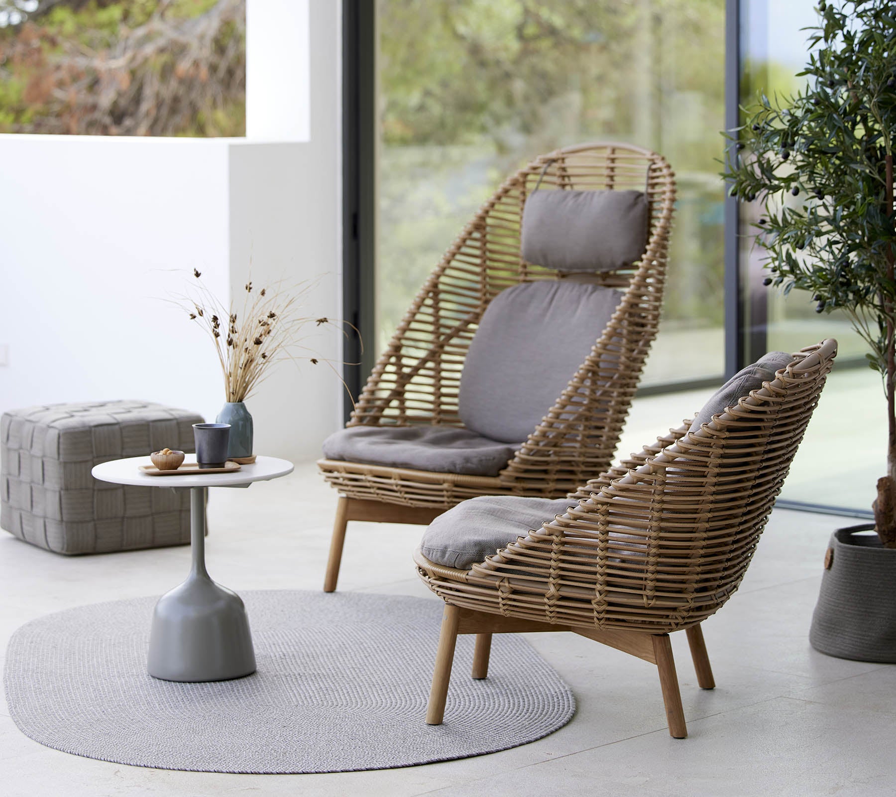 Two stylish woven chairs with cushions, accompanied by a small round table and decorative elements, set on a circular rug.
