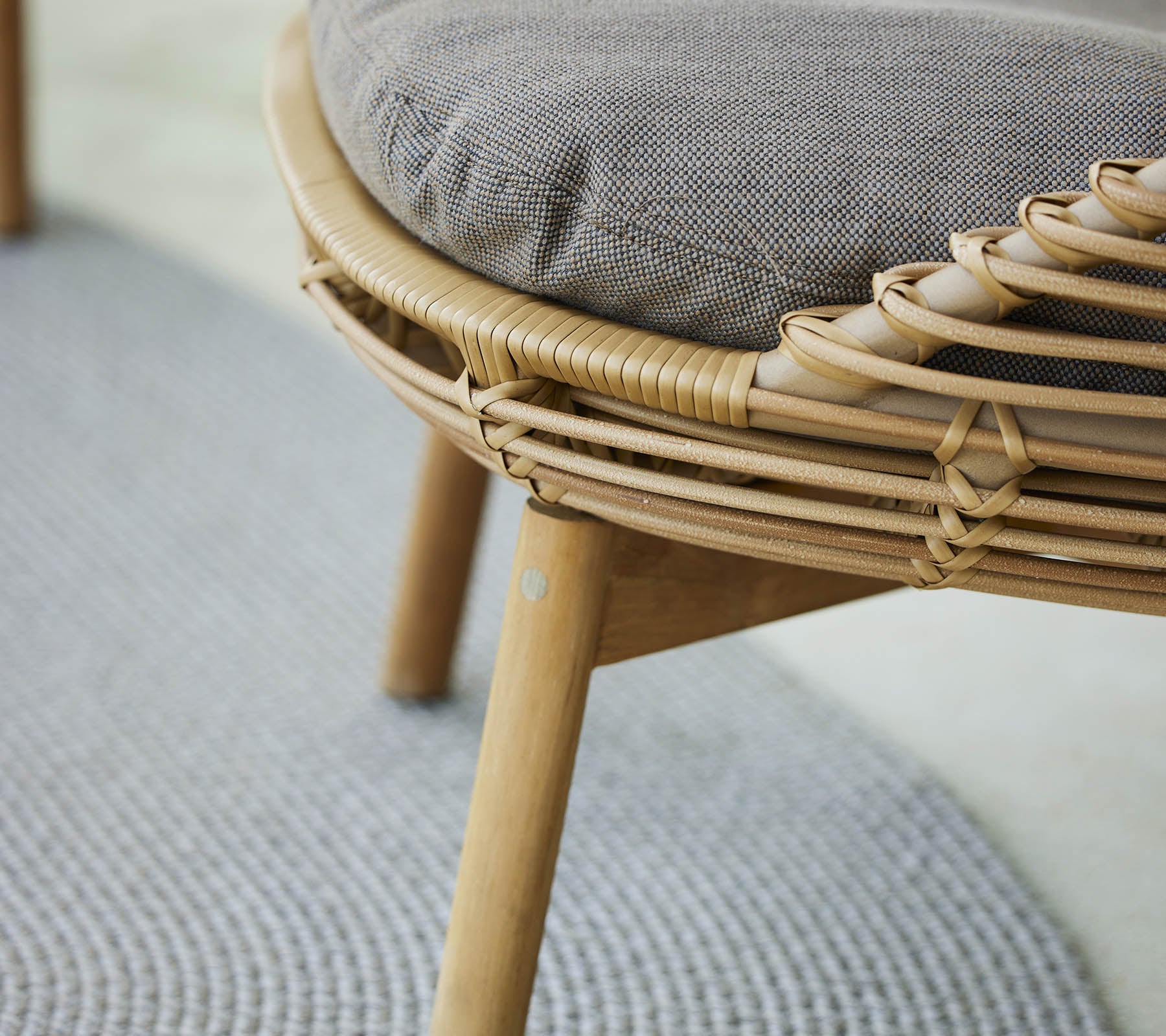 A close-up view of a stylish lounge chair featuring a woven frame and a cushioned seat, complemented by a textured rug below.