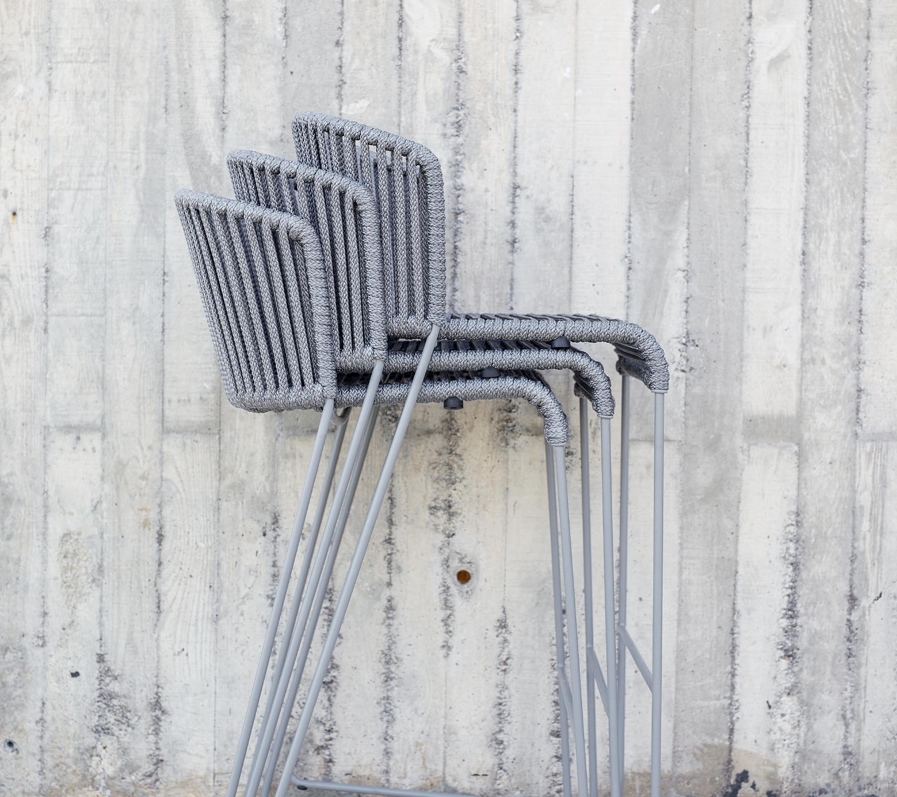 Stacked grey chairs against a textured concrete wall.