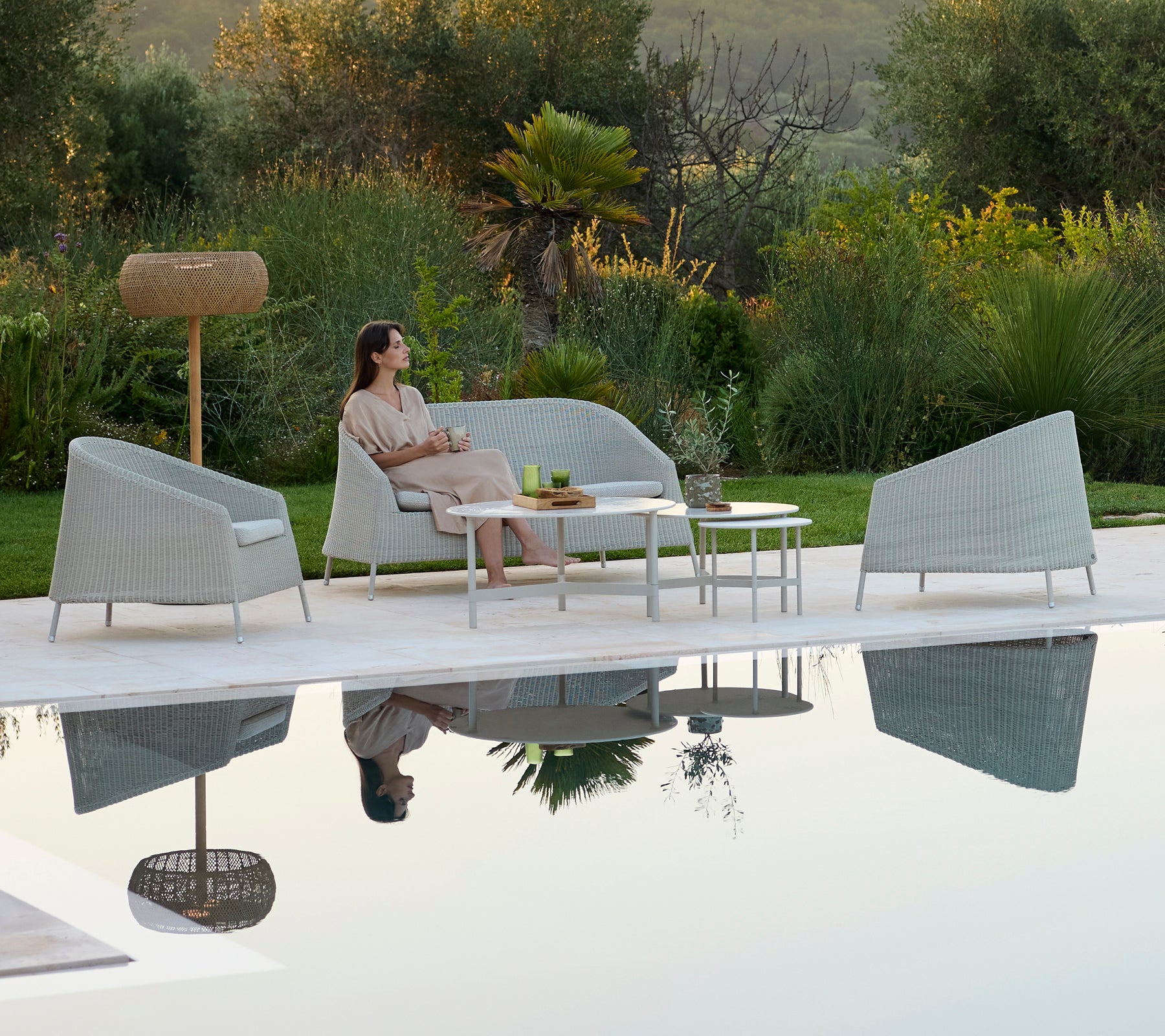 Modern grey sofa and armchairs surrounding a white table in a relaxing outdoor lounge.