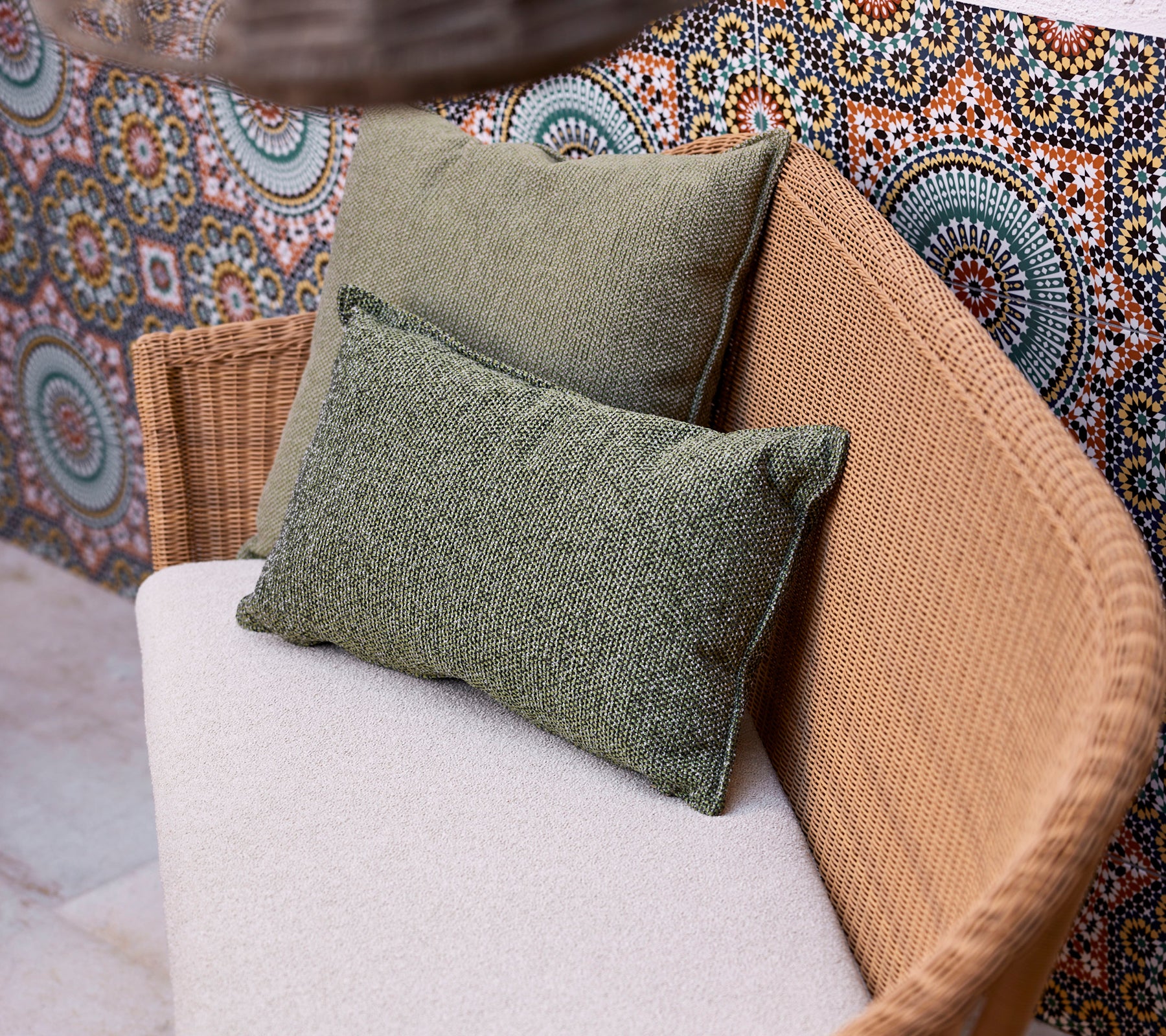 Two green scatter cushions on a light-colored sofa, positioned against a vibrant, patterned backdrop featuring circular designs.