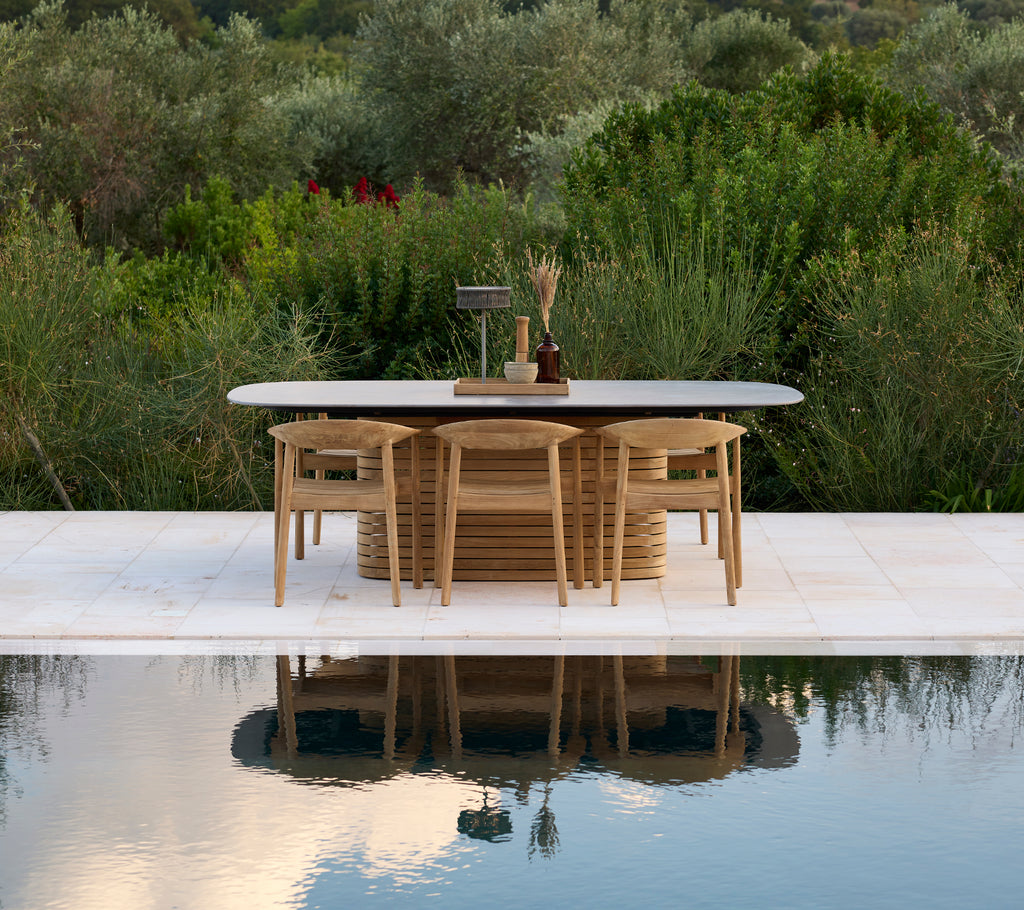 Modern outdoor table with chairs by a pool and surrounded by greenery.