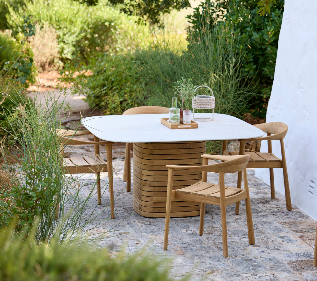 Modern outdoor setting featuring a white table and wooden chairs surrounded by greenery.
