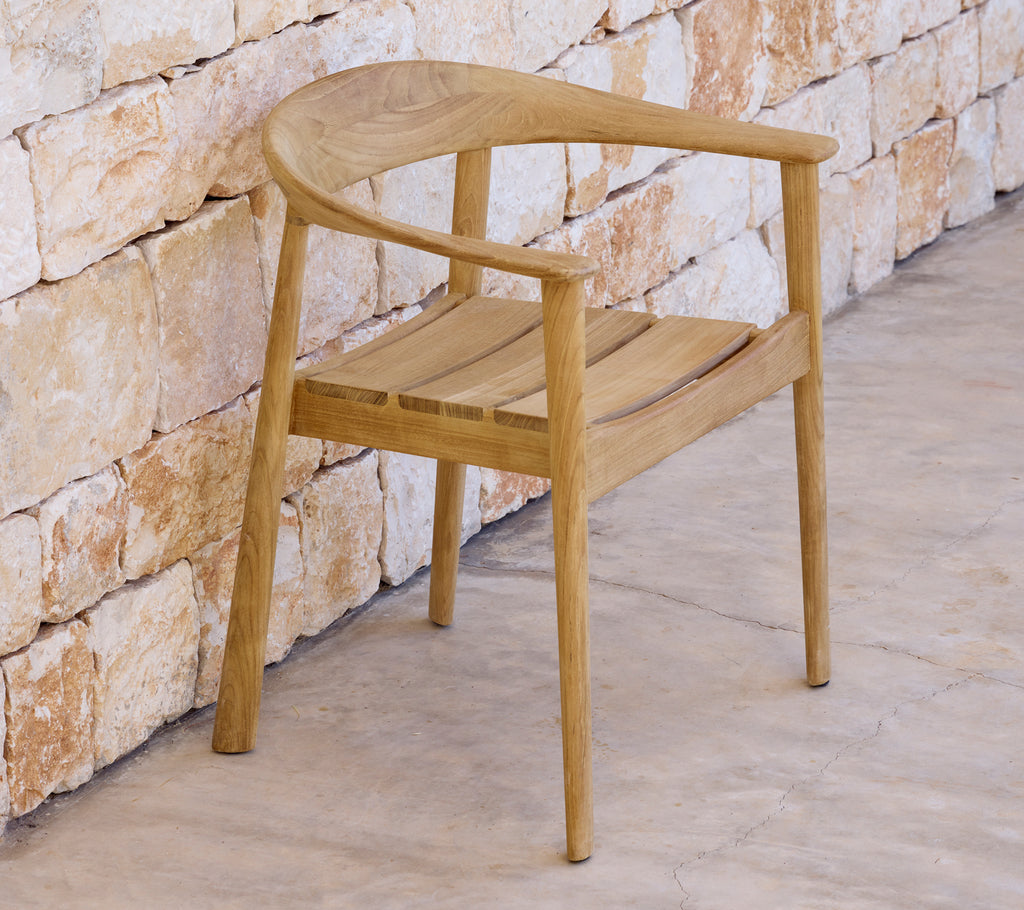 Modern wooden chair beside a stone wall in a minimalist setting.