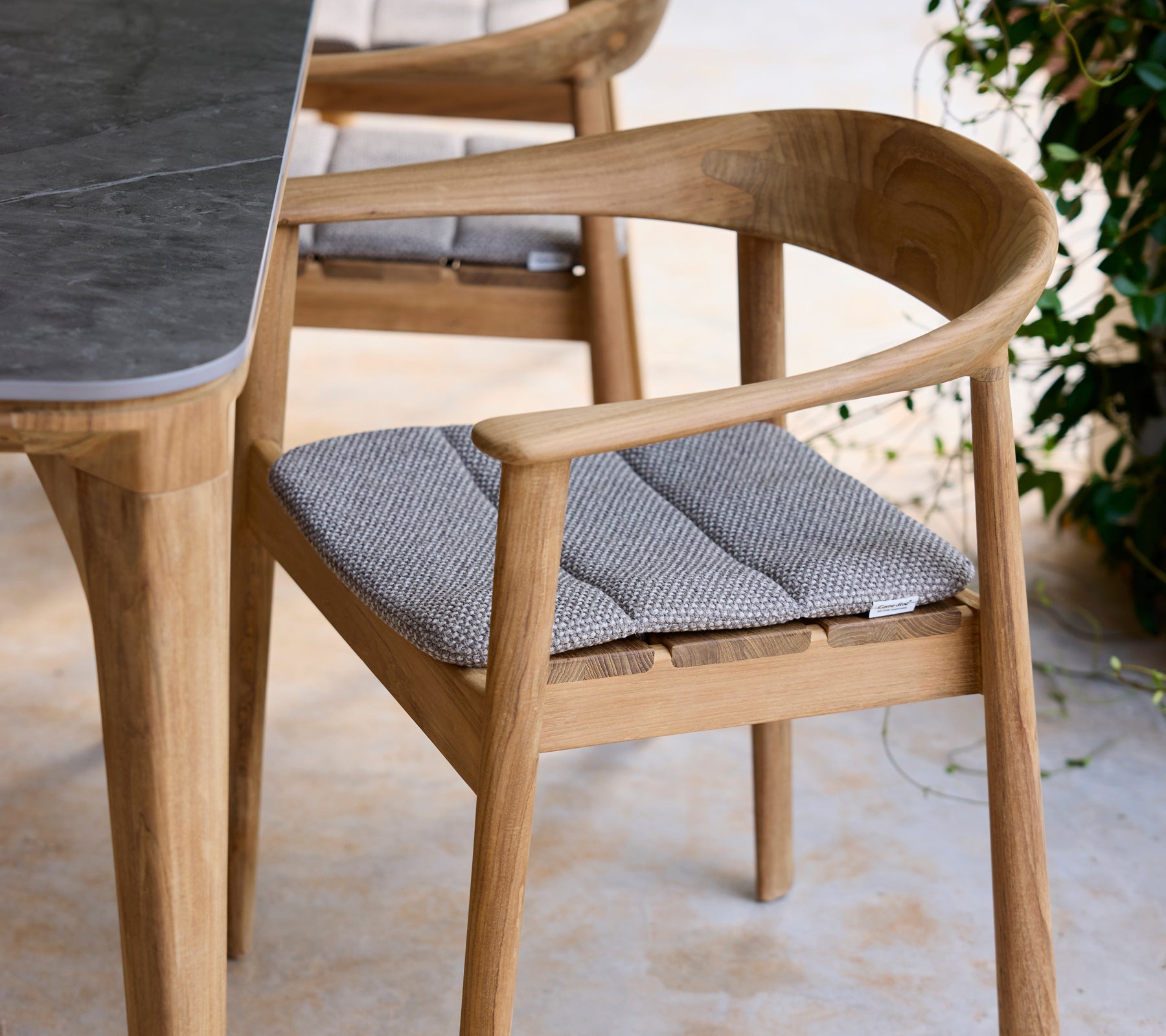 Modern wooden chair with grey cushion next to a table in a lounge setting.