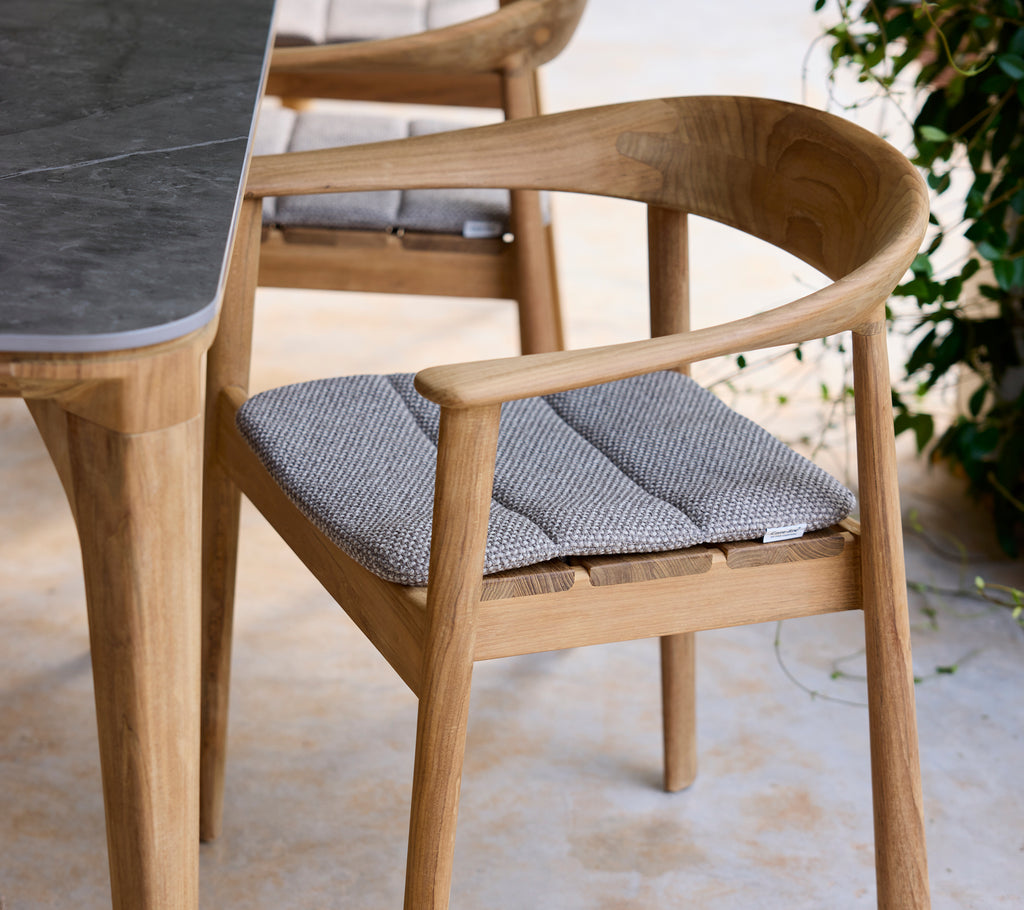 Modern wooden chair with grey cushion next to a table in a lounge setting.