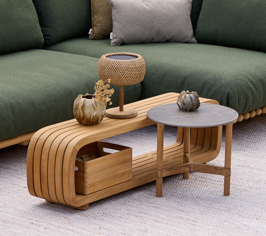 Modern wooden coffee table with a grey side table, lamp, and decorative vase in a lounge setting.
