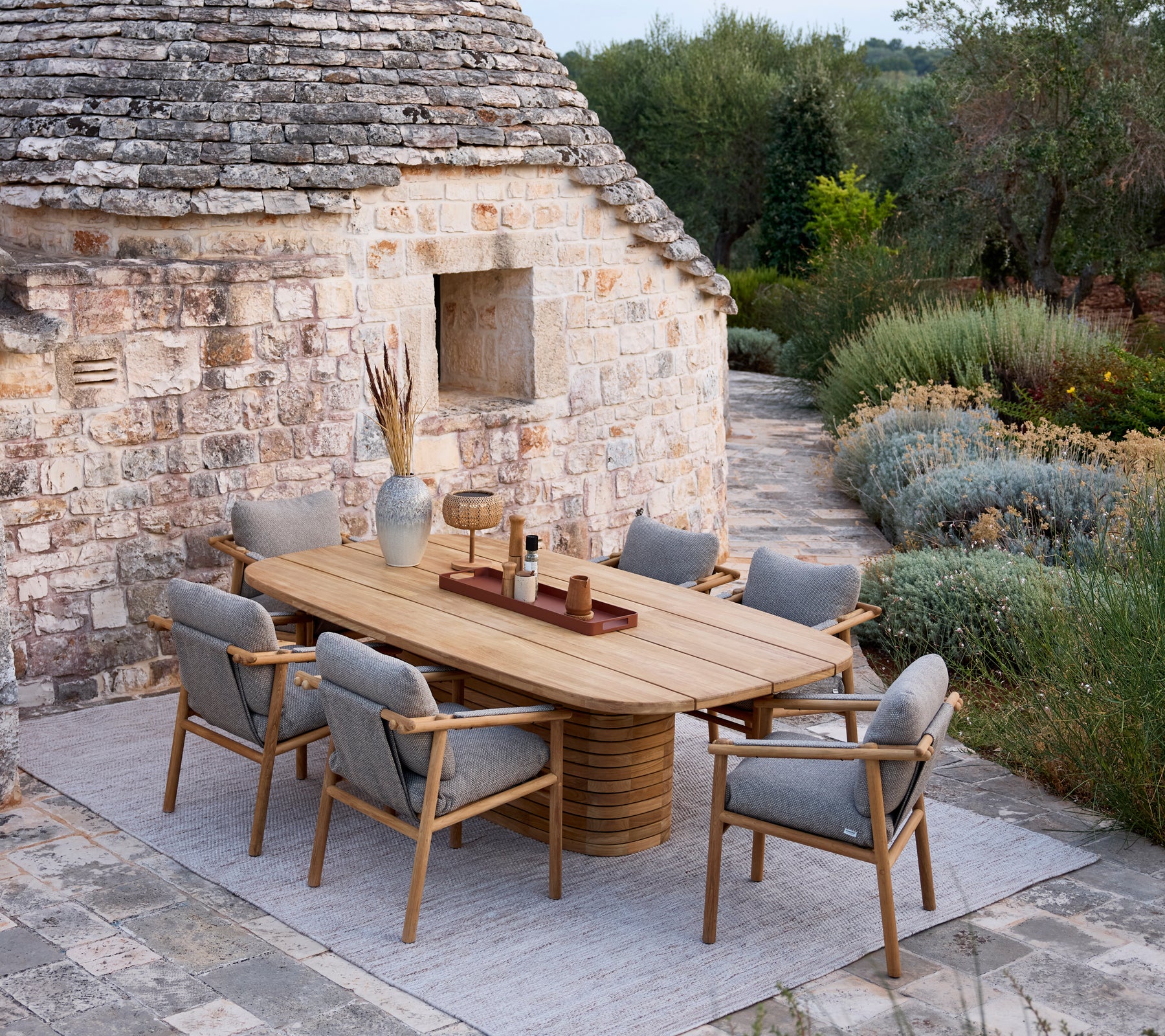 Wooden dining table with grey cushion chairs in a rustic outdoor setting.