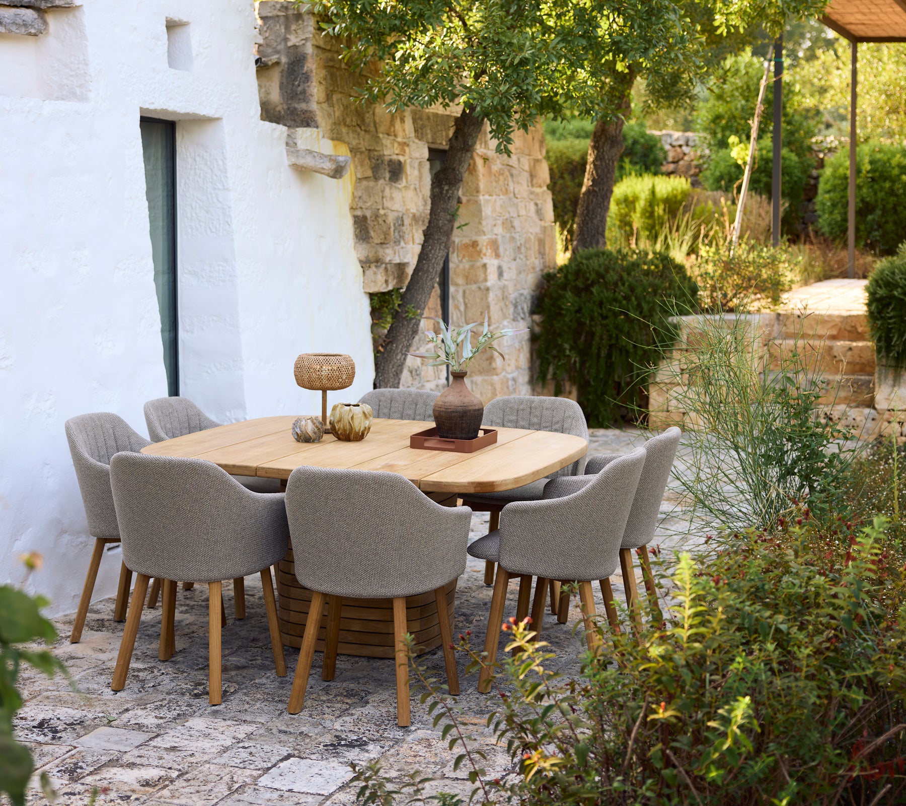 Modern wooden dining table surrounded by grey chairs in a garden setting.